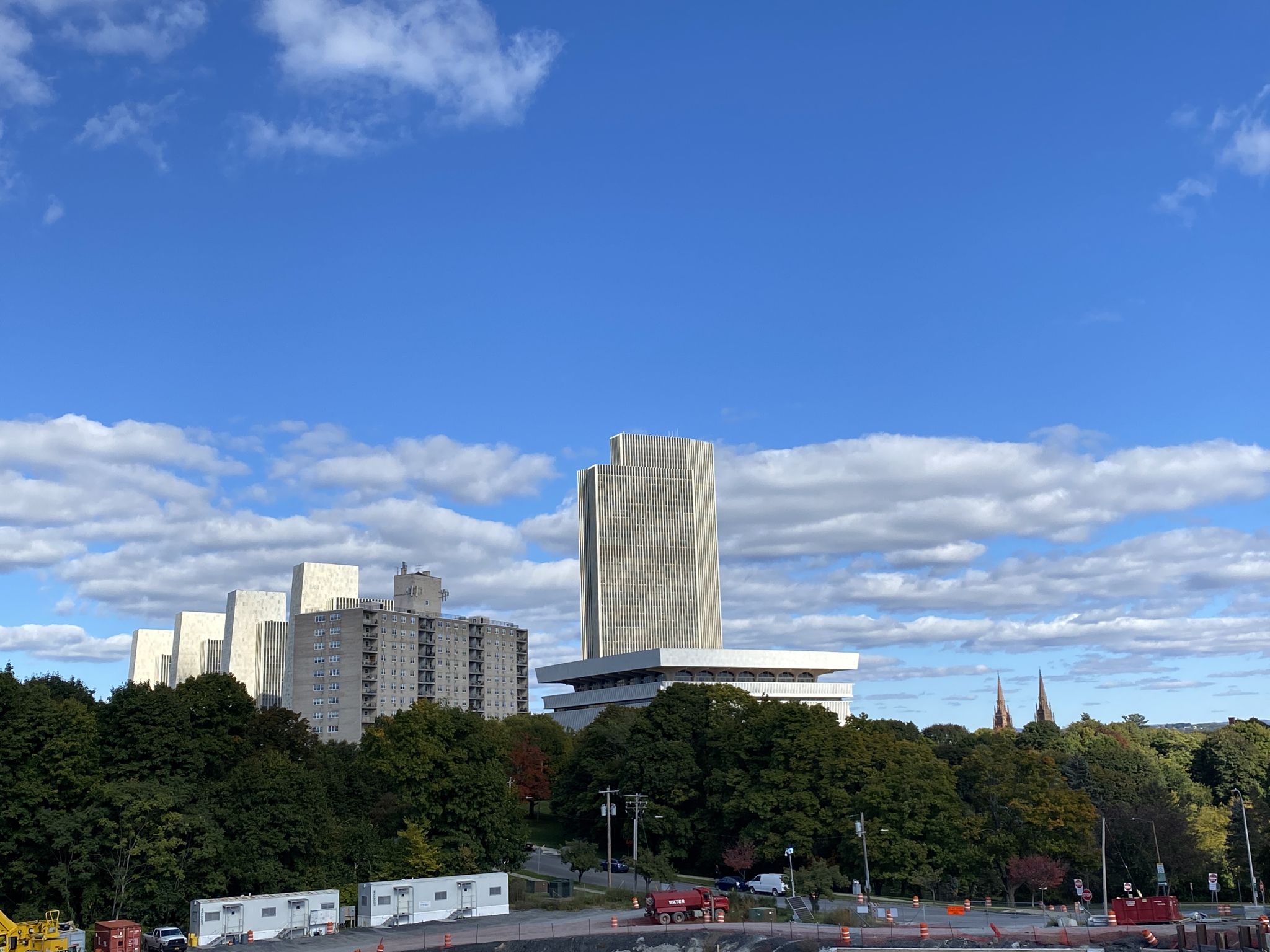 Modern buildings rise above green trees under a bright, cloudy sky. - Lincoln Park loop