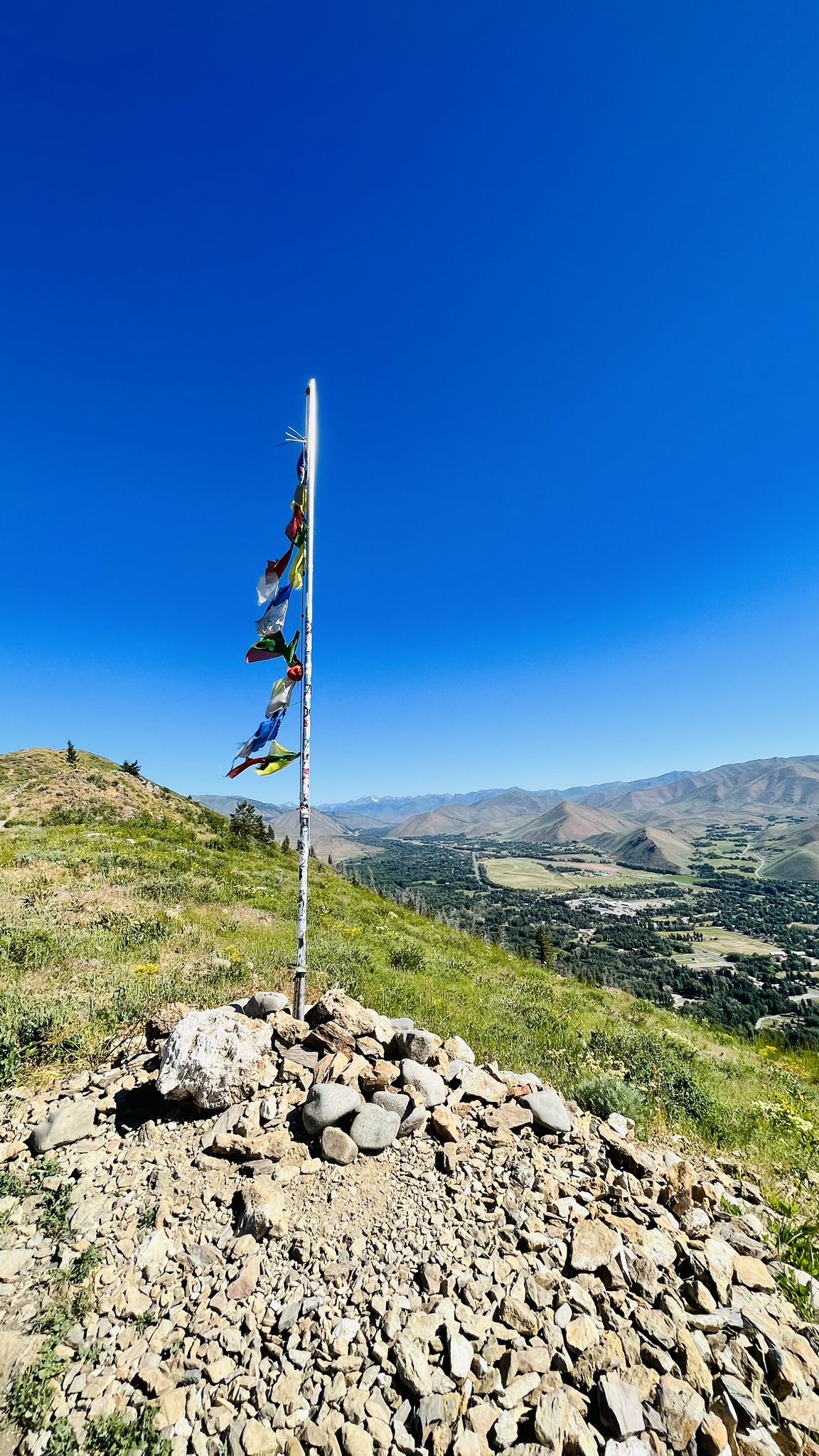 Colorful flags on a rocky cairn atop a sunny hill overlooking a valley. - Carbonate Mountain Trail