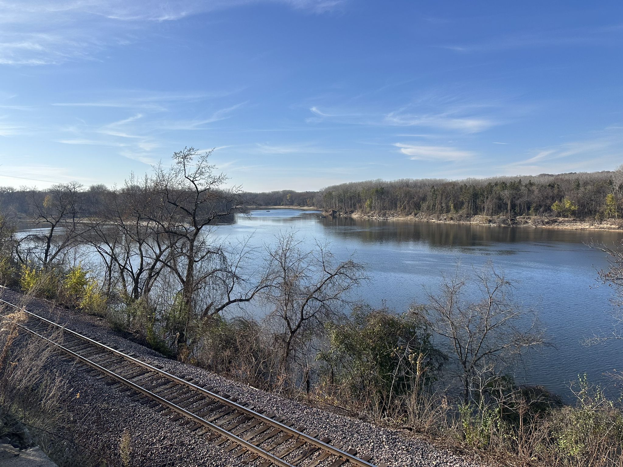 Wide river with bare trees on banks, railroad tracks in foreground, clear sky. - Big Rivers Regional Trail