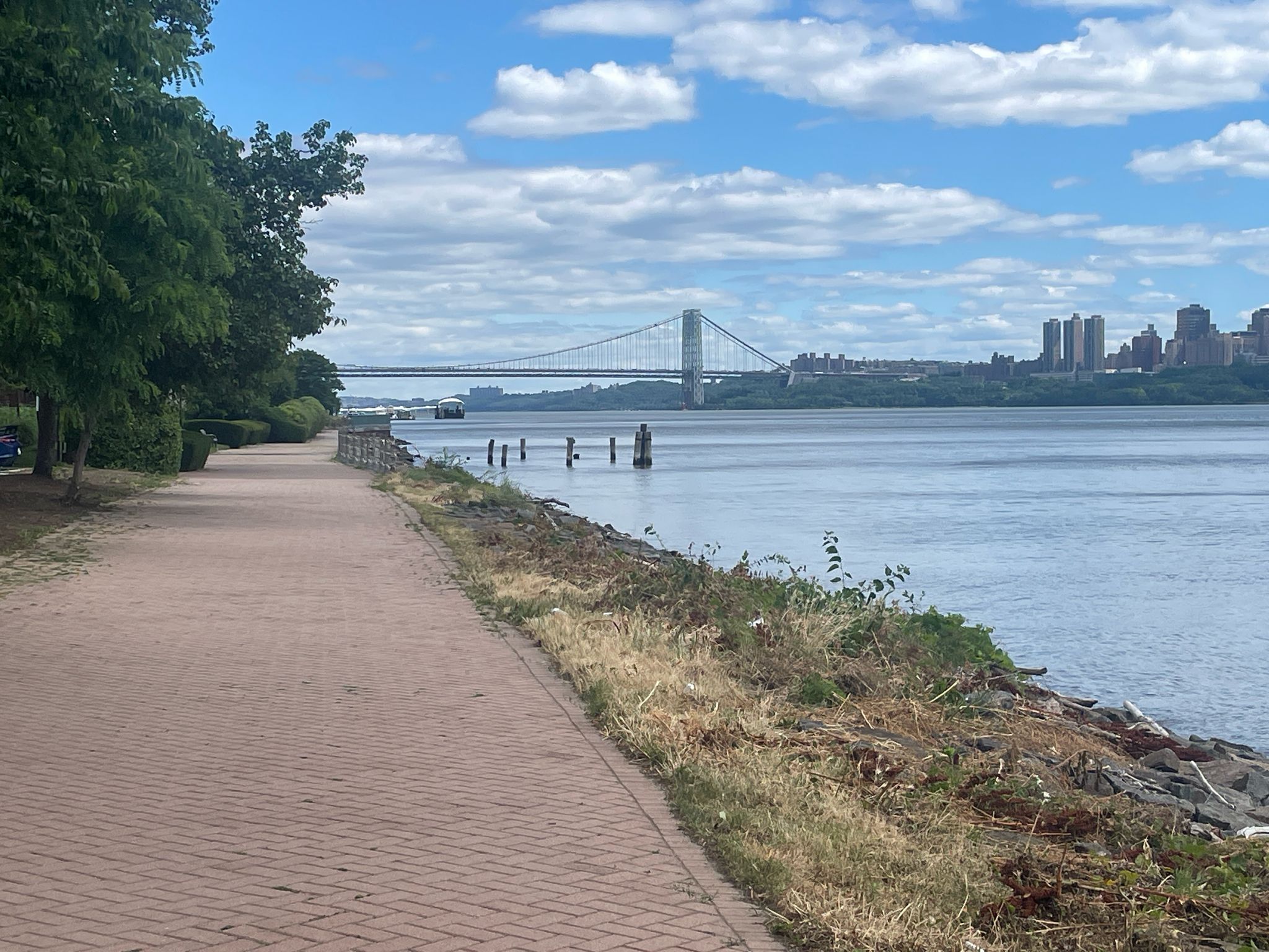 Paved path alongside a river with a distant bridge and city skyline. - Hudson River Waterfront Walkway: Edgewater