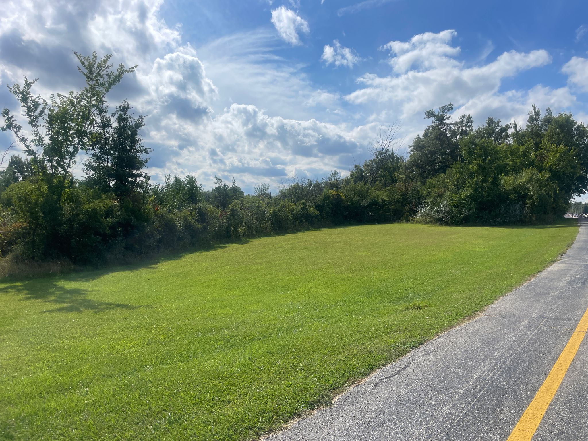 Expansive green lawn next to a paved road under a bright, cloudy sky. - Tinley Creek Purple Paved Trail Loop