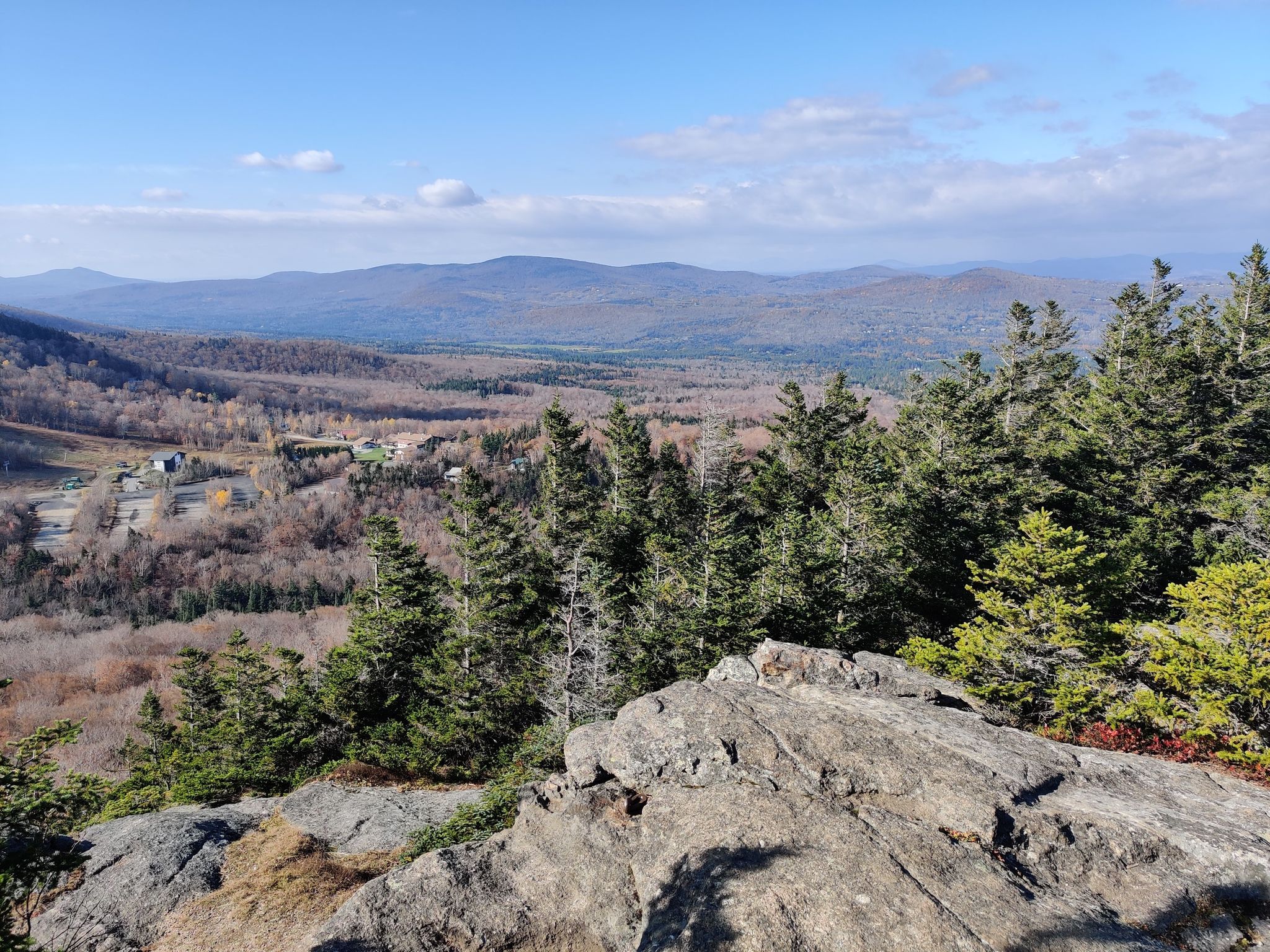 Sunny mountain vista with rocky foreground, evergreen trees, and distant autumn valley. - Bald Mountain