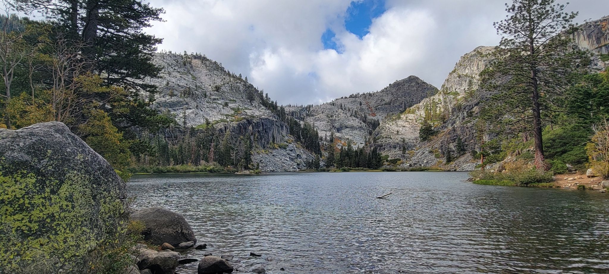 Calm lake surrounded by rocky, forested mountains under a cloudy sky. - Eagle Falls Trail