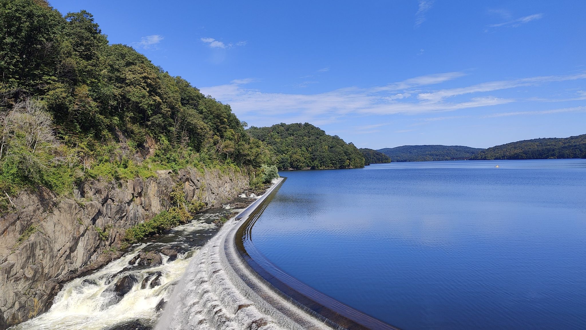 Water cascading over a dam into a wide lake, surrounded by green hills. - Peekskill Waterfront Park – New Croton Dam loop from New Croton Dam