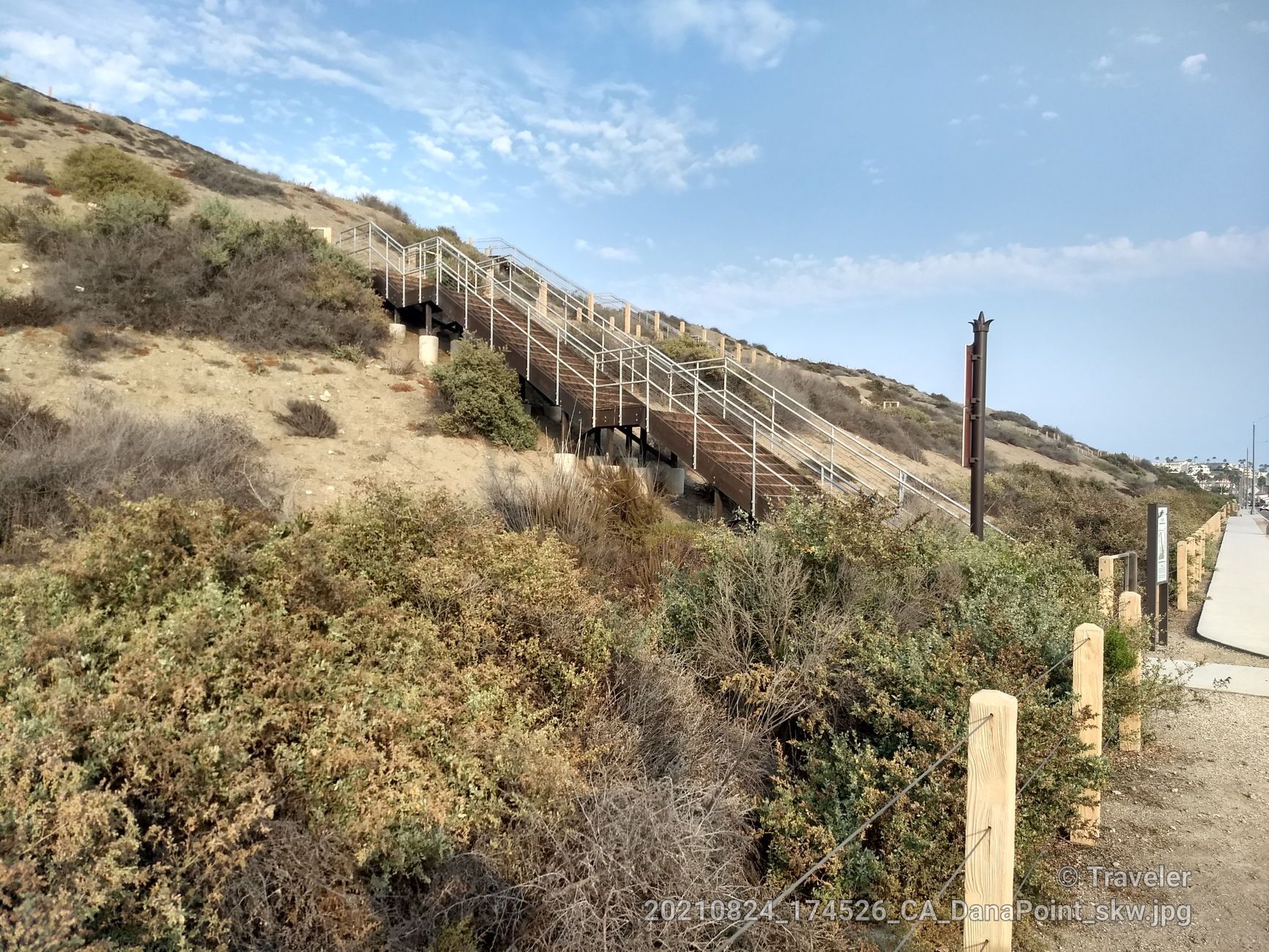 Long wooden stairs with railings ascend a dry, brush-covered hillside under a cloudy sky. - North Beach – Doheny State Beach loop from Bay Cliff Village