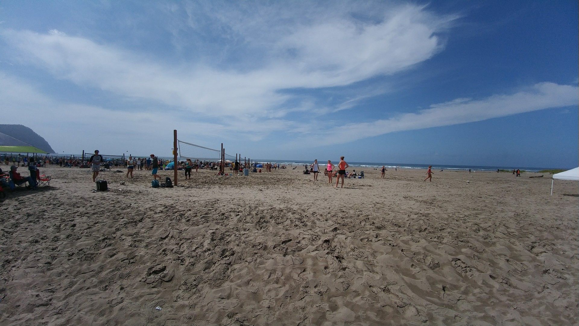 Crowded sandy beach with multiple volleyball nets and people playing under a blue sky. - Oregon Coast Trail: Seaside Promenade