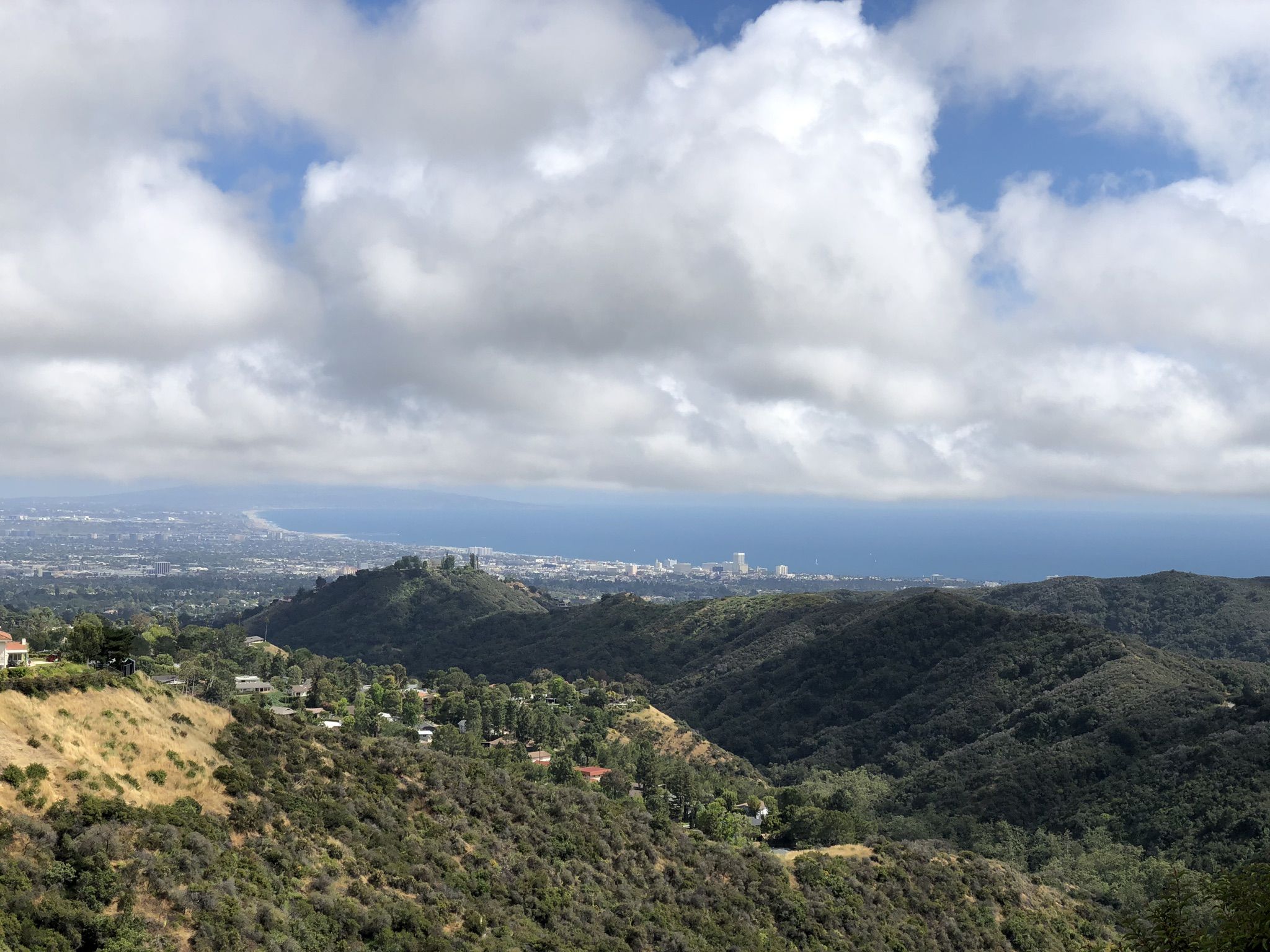 Hilly landscape with distant city and ocean under a partly cloudy sky. - "West Mandeville Fire Road and Ridge Trail"