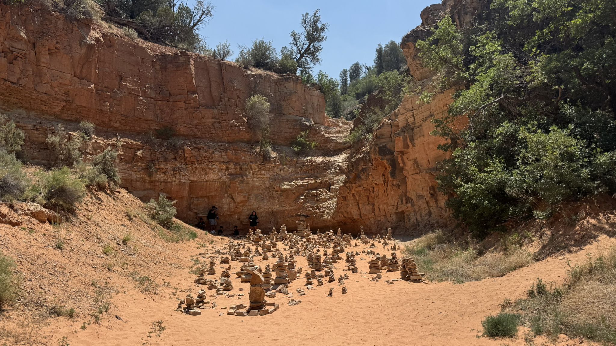 Sandy canyon floor filled with numerous rock cairns under bright sunlight. - Belly of the Dragon Trail