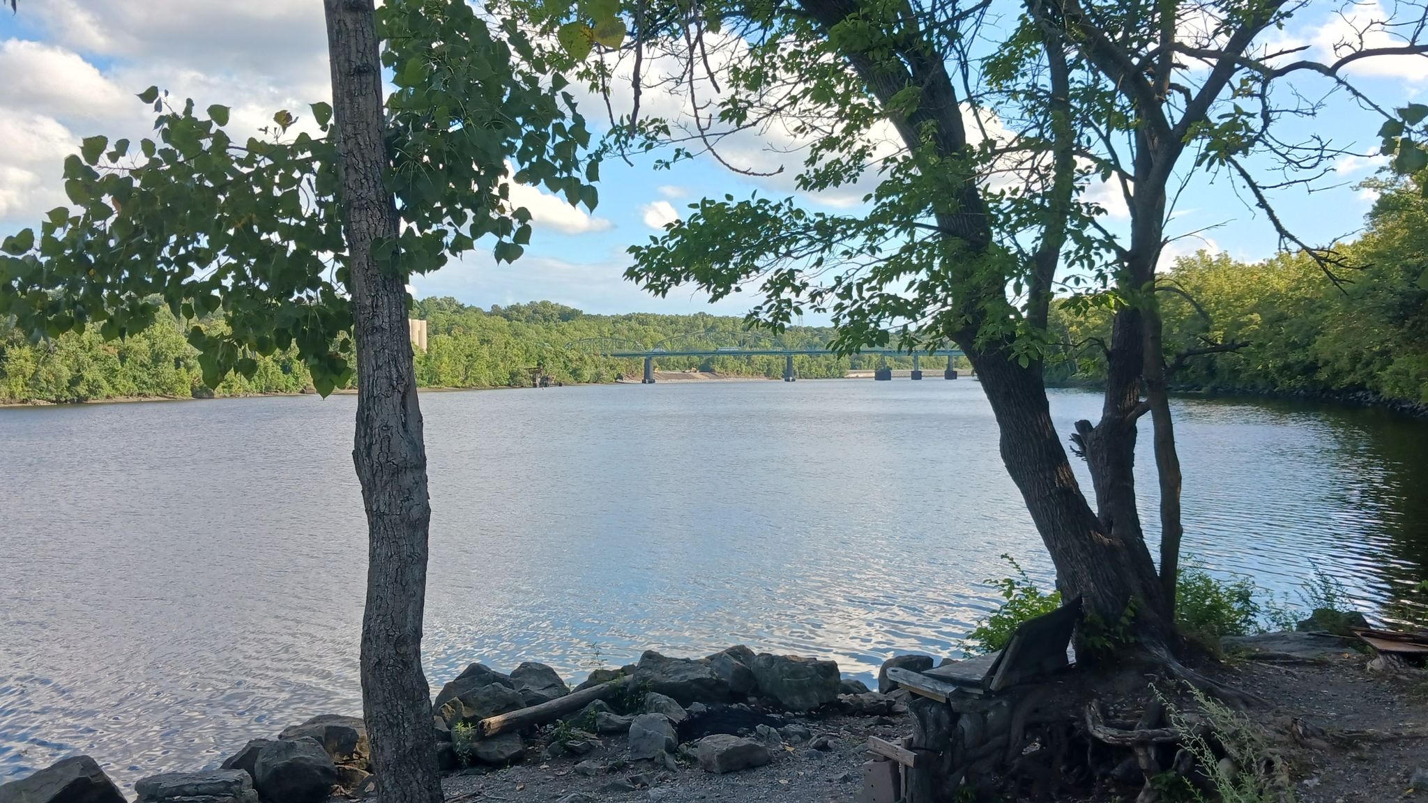 Wide river with a distant bridge, framed by trees and a rocky shore. - Mohawk-Hudson Trail Tunnel loop from Troy