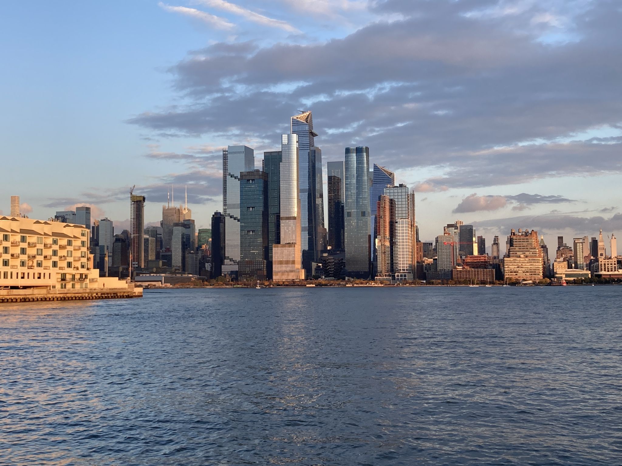 Modern city skyline across a wide river under a clear blue sky. - Weehawken Cove – Port Imperial Waterfront loop from Hoboken