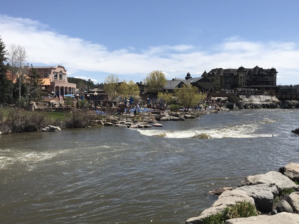 Bright daylight view of a river flowing past buildings and people. - San Juan Riverwalk Overlook loop from Pagosa Springs