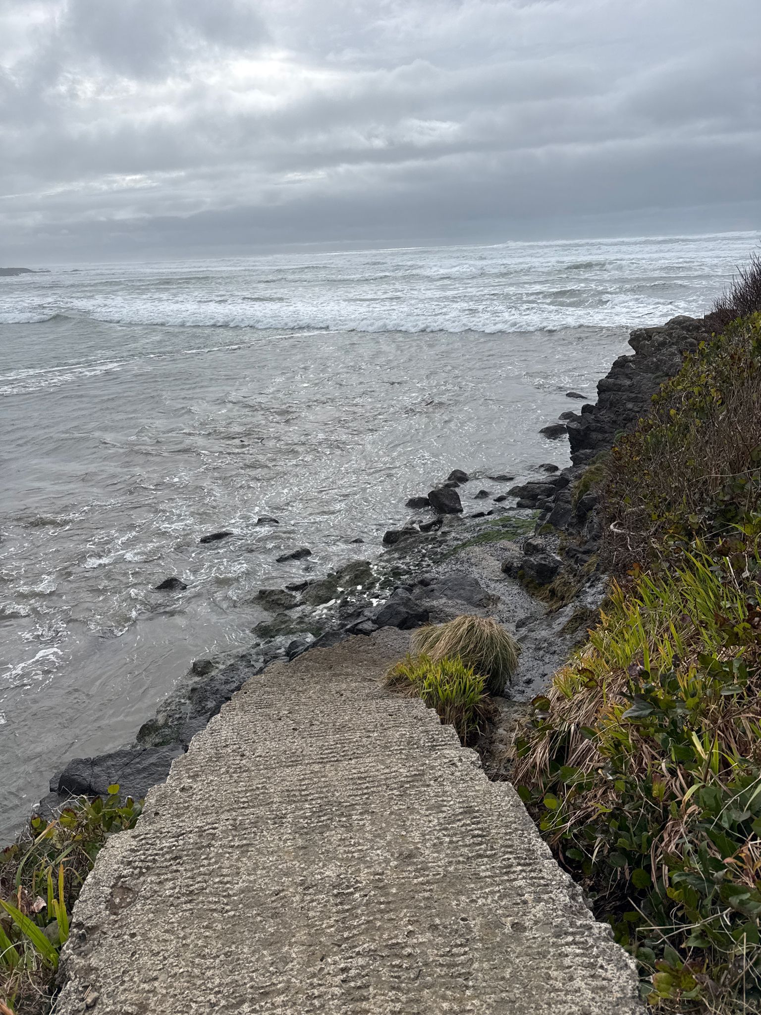 Concrete ramp descends into a grey, wavy ocean under an overcast sky. - Yachats State Recreation Area – Yachats loop from Yachats Ocean Road State Natural Site