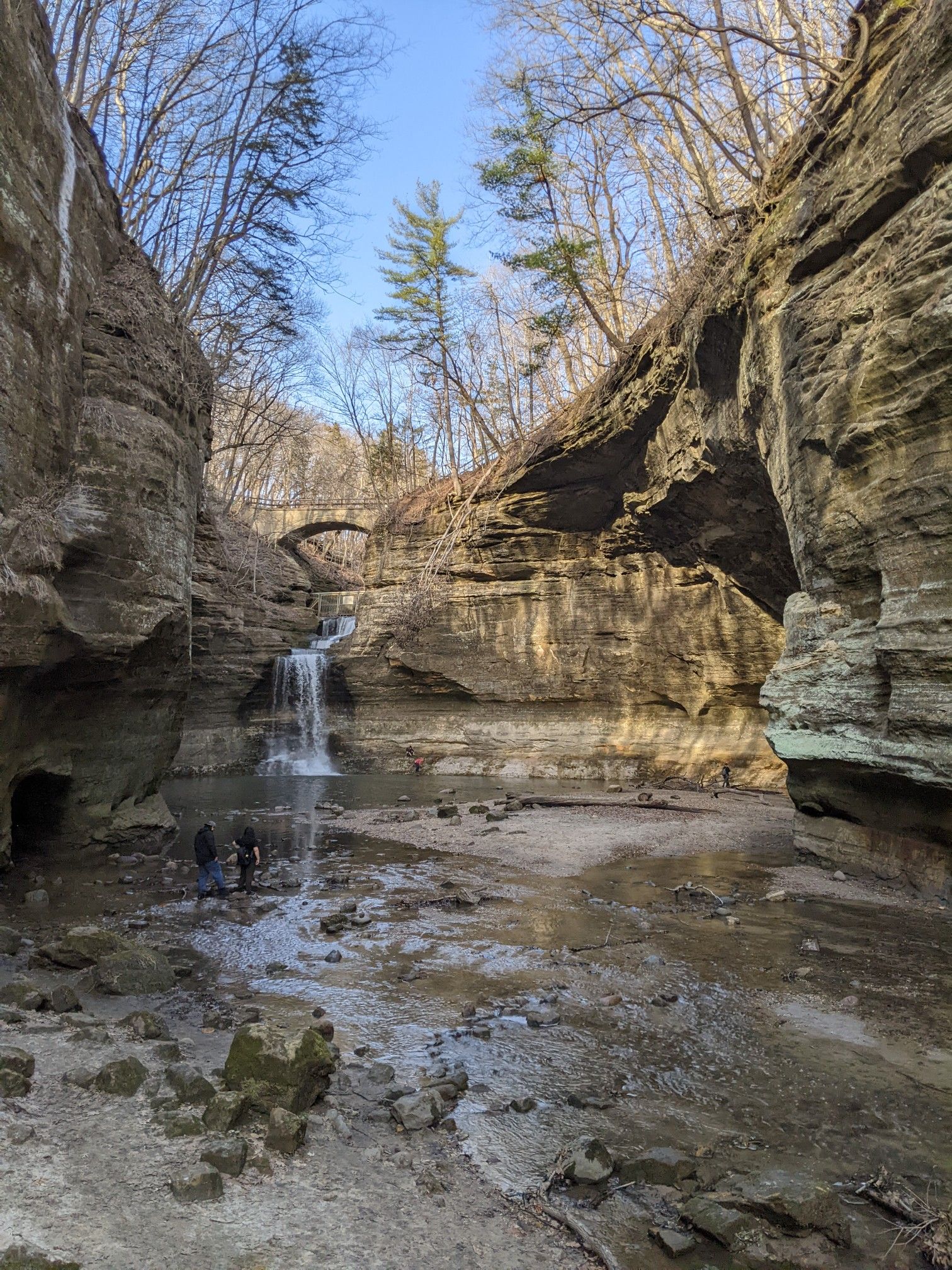 People stand in a rocky canyon with a small waterfall and stream under blue sky. - Cascade Falls loop from Matthiessen State Park
