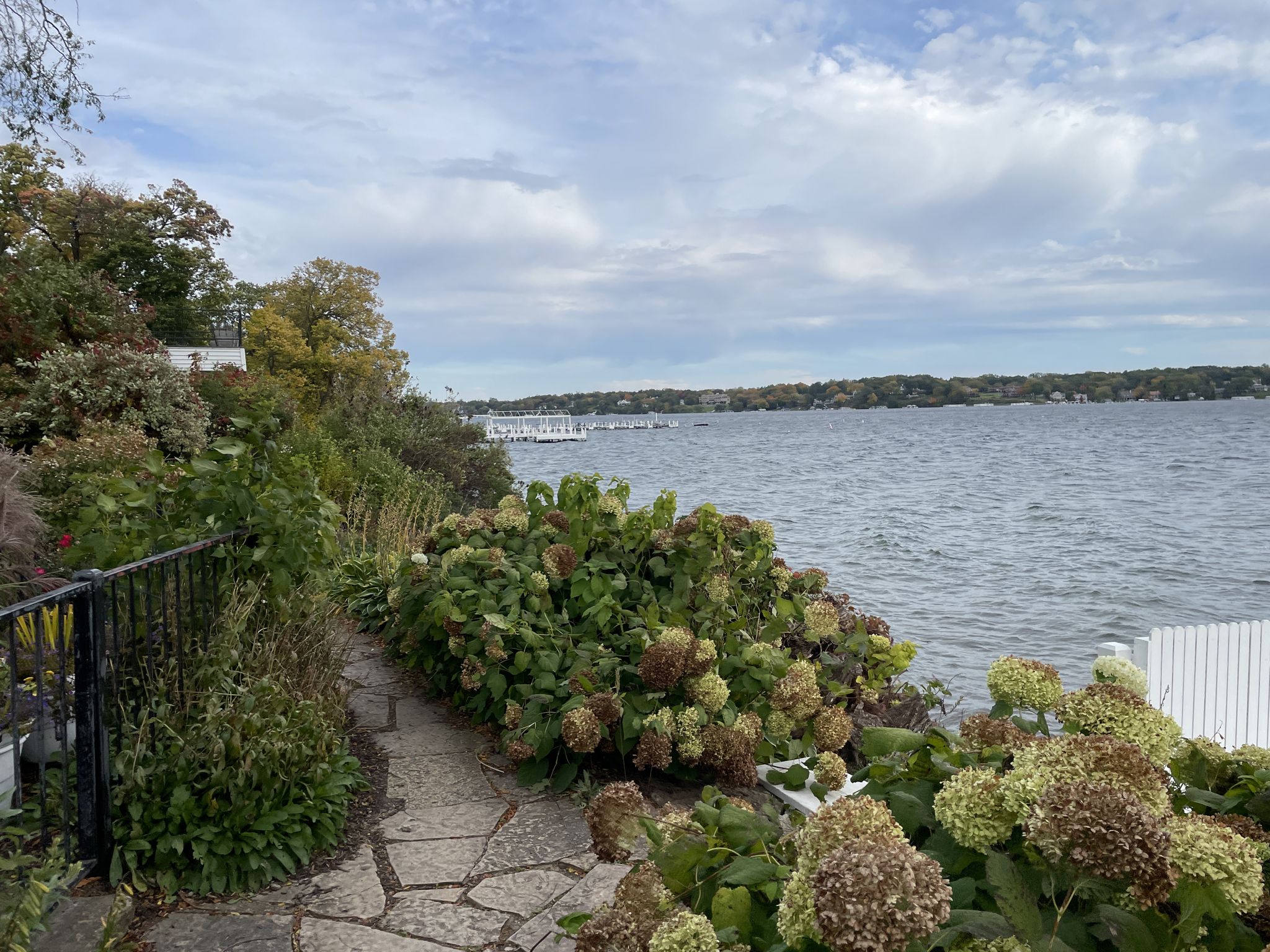 Stone path winding along a landscaped lake shore with hydrangeas and distant docks. - Cisco Bay loop from Lake Geneva