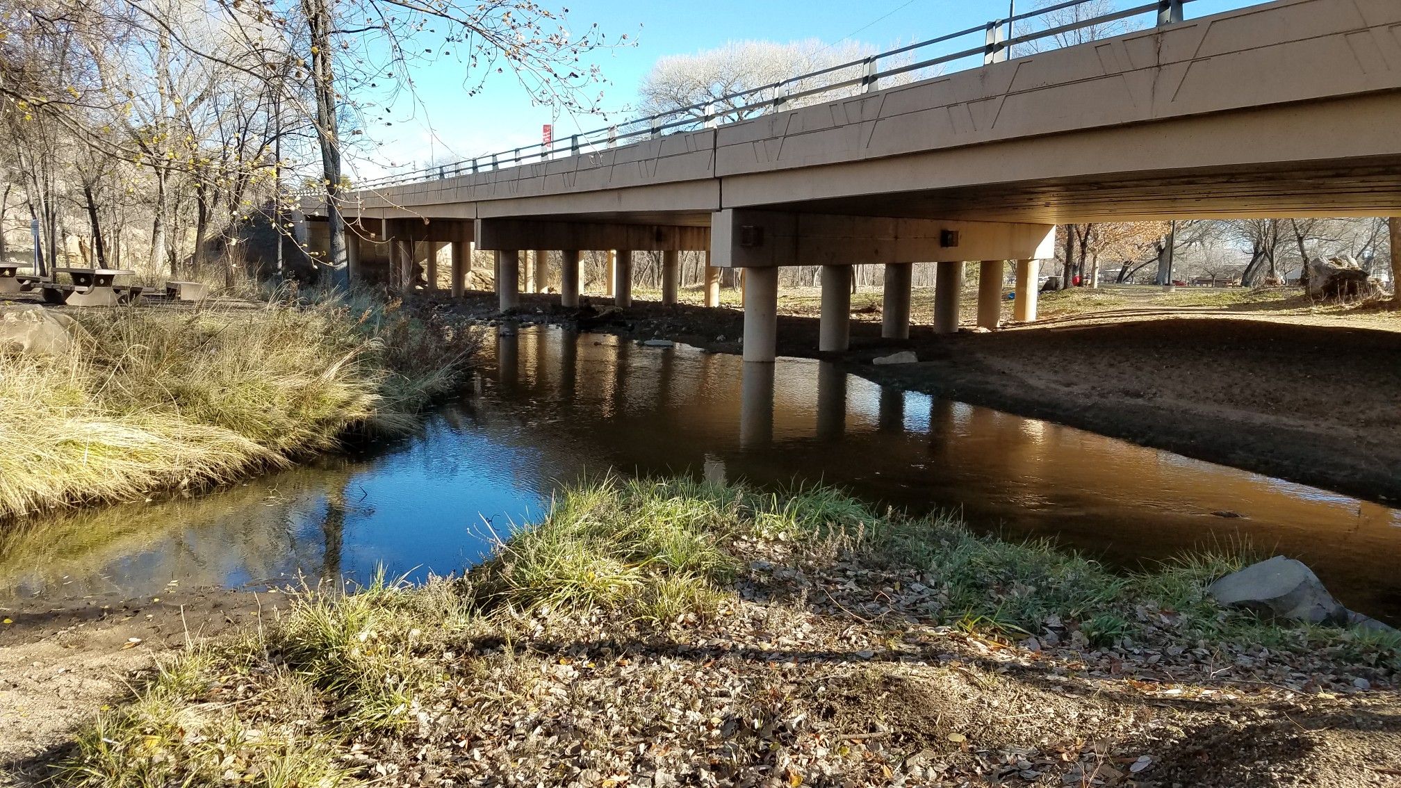 A river flows under a concrete bridge on a bright, sunny day. - Montezuma Promenade