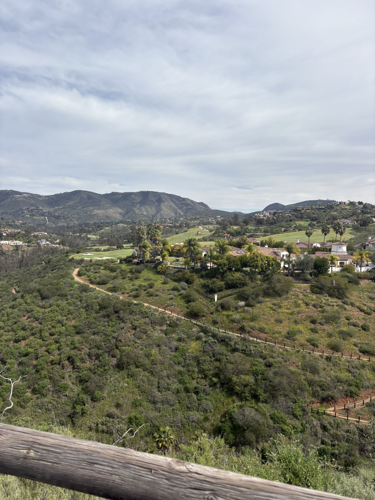 Overlook of a green valley with houses, a golf course, and distant mountains. - Santa Fe Valley Trail