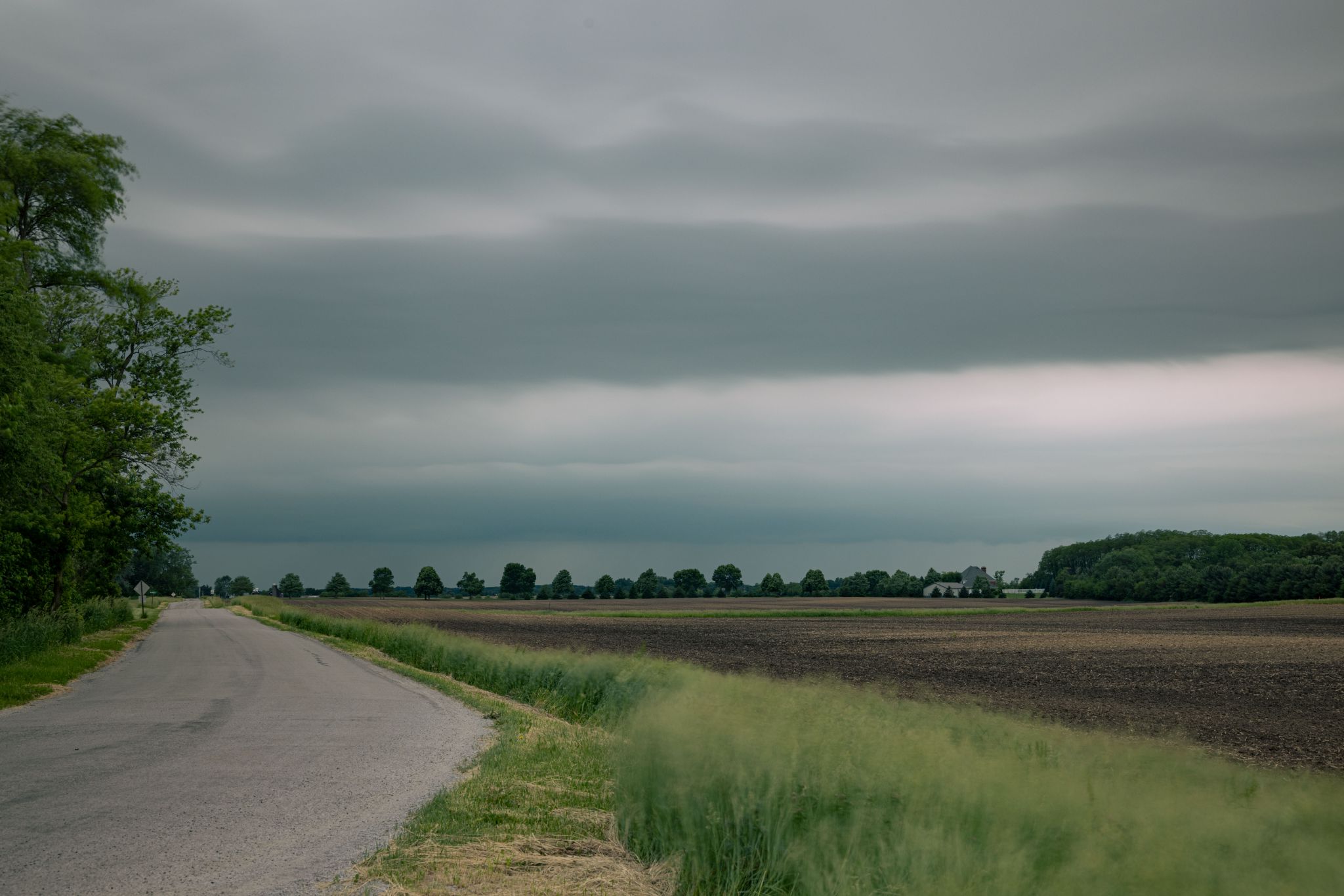 A rural road next to a field under dark, cloudy skies. - Little Calumet River – Erie-Lackawanna Rail-Trail loop from East Chicago