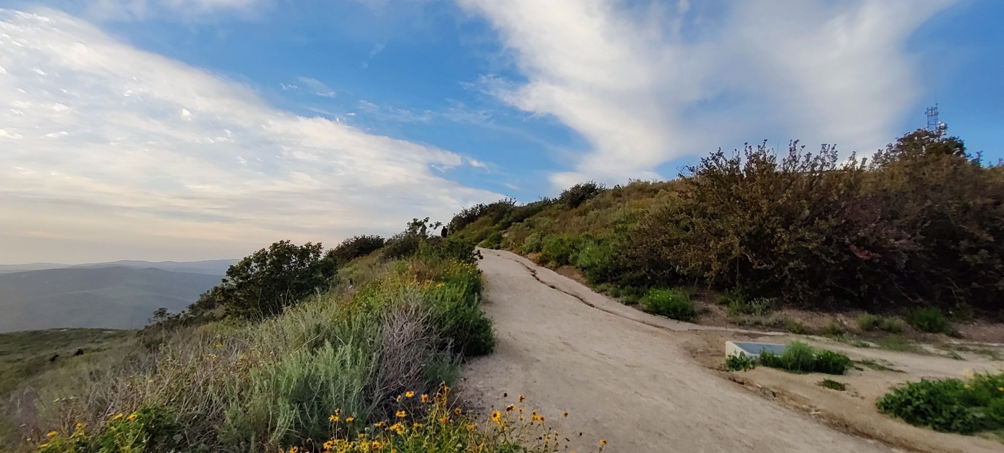 A dirt path winds up a brush-covered hill under a partly cloudy sky. - West Ridge and Wood Canyon Loop