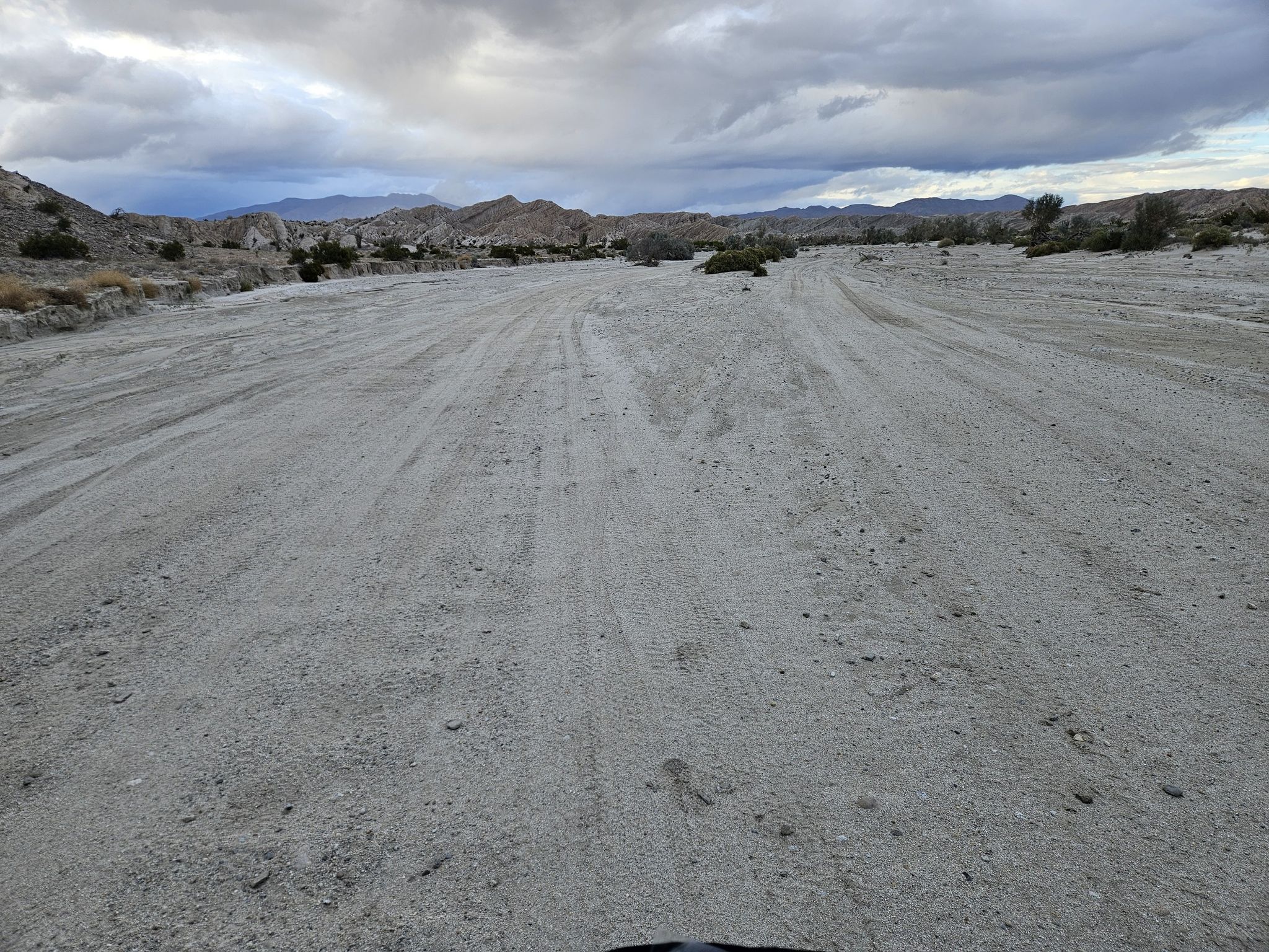 Wide sandy desert road with distant mountains under an overcast sky. - Arroyo Tapiado Mud Caves Trail