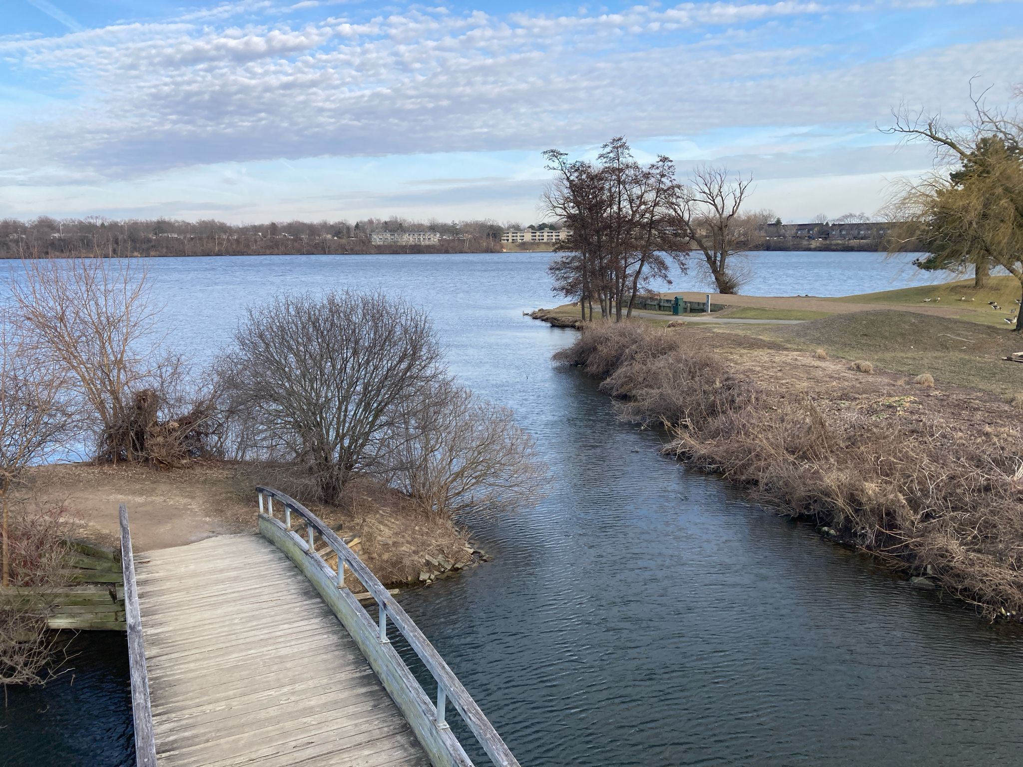 Wooden bridge over a narrow river leading to a wide lake under a cloudy sky. - Iron Belle and Border-to-Border Trail Loop