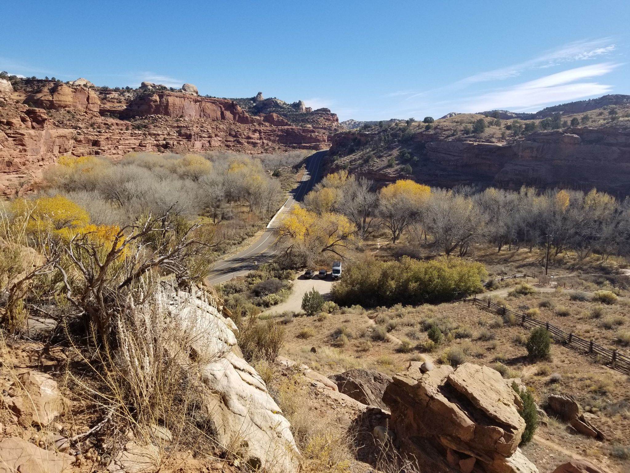 Sunny desert canyon with a winding road, autumn trees, and rocky cliffs. - The 100 Hands Pictographs