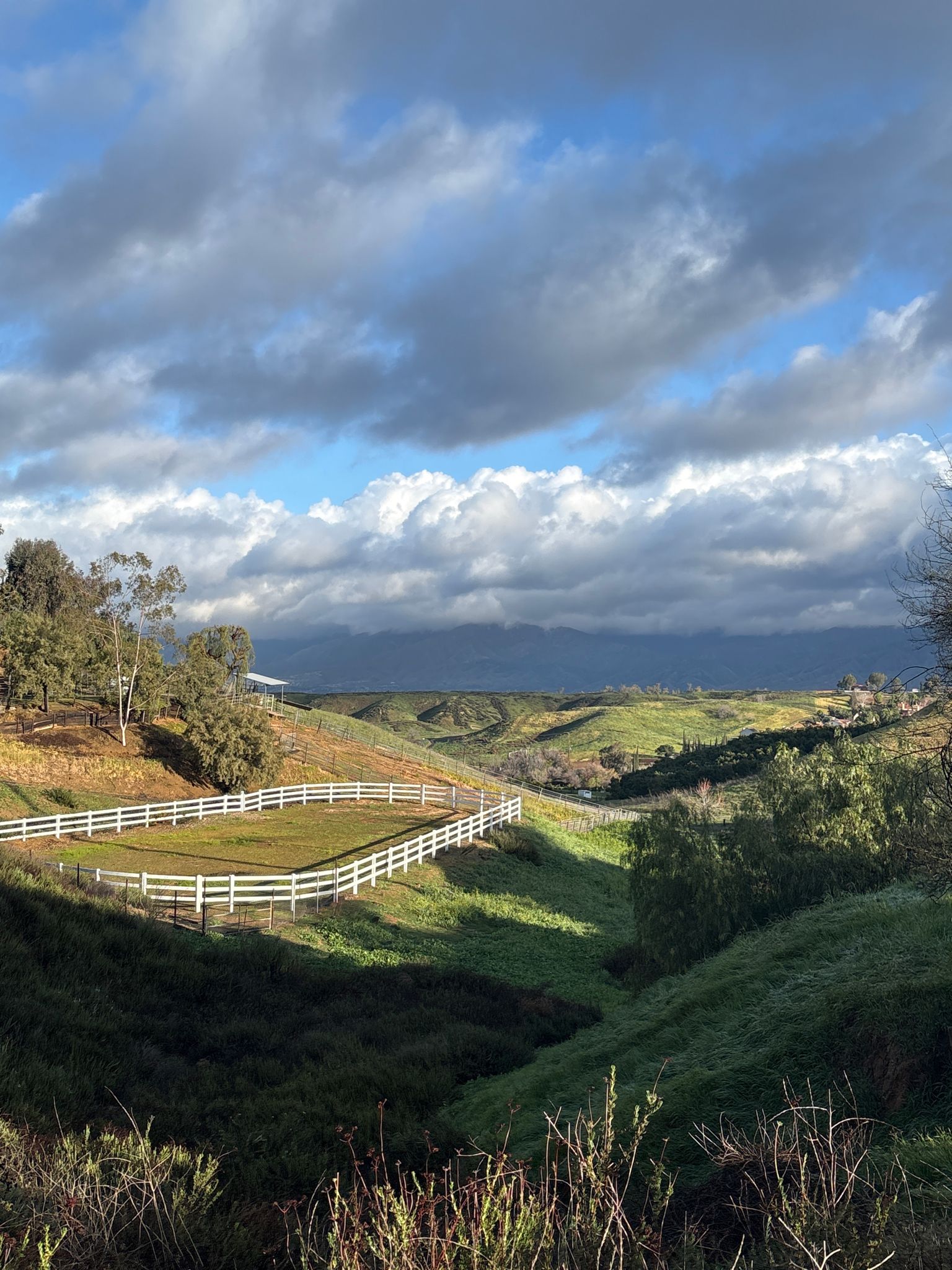 Green rolling hills with a white fence under a dramatic, cloudy sky. - Oak Glen loop