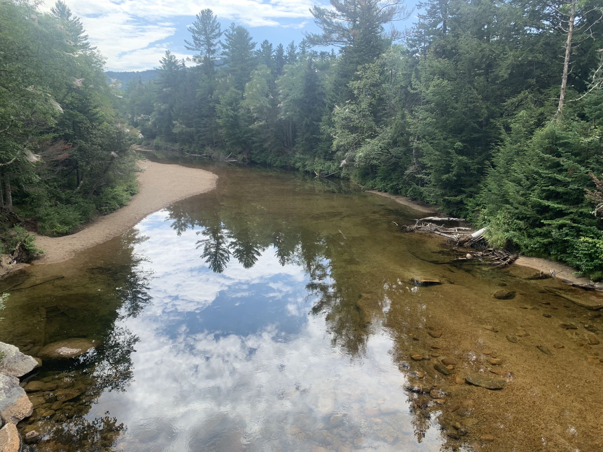 Calm river reflects cloudy sky, bordered by sandy banks and green forest. - Bartlett Village Gazebo Park – Bear Notch Road loop from Bartlett