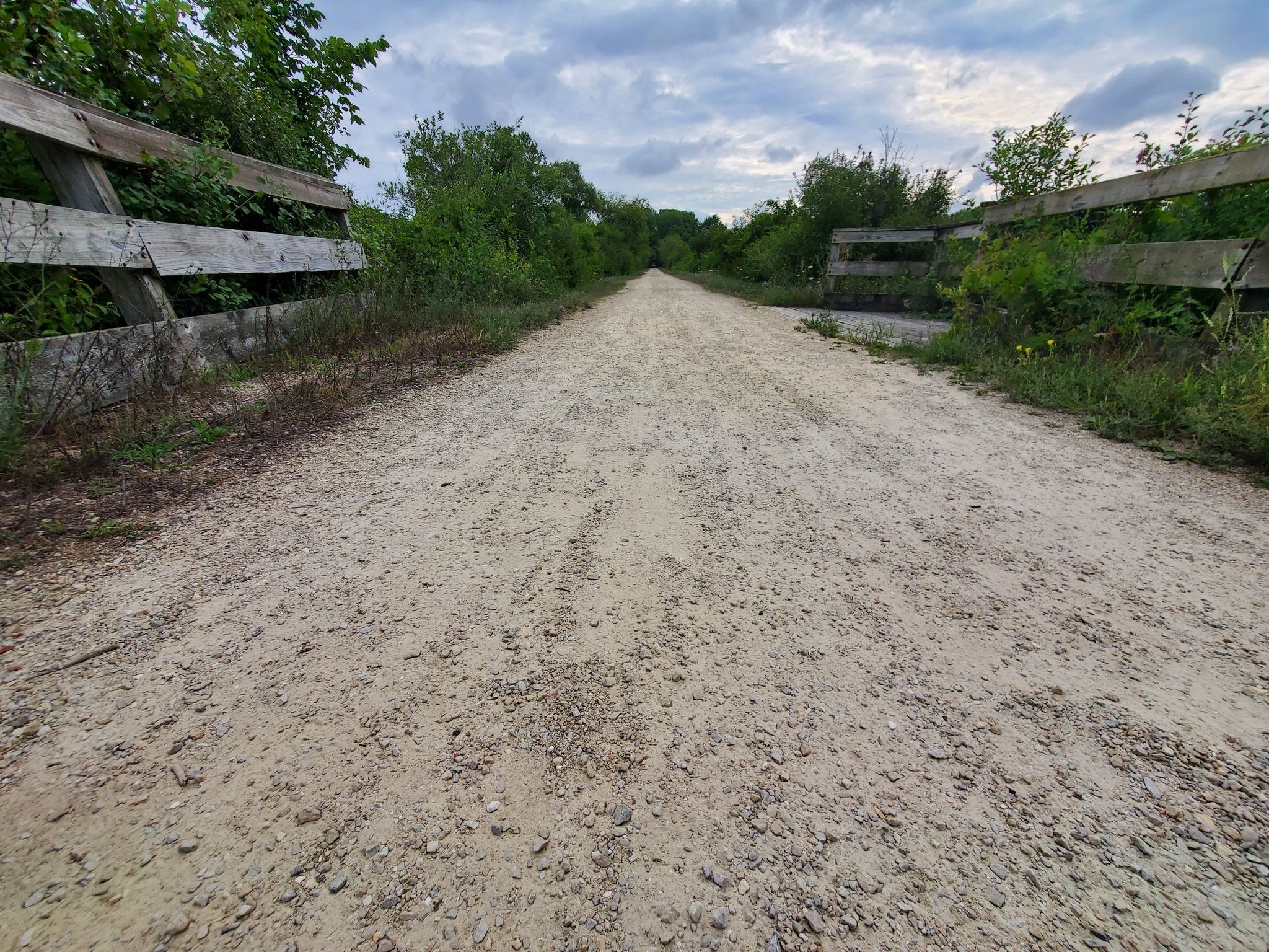 Wide dirt path between wooden fences and dense green foliage. - Kettle Moraine and Glacial Drumlin Loop