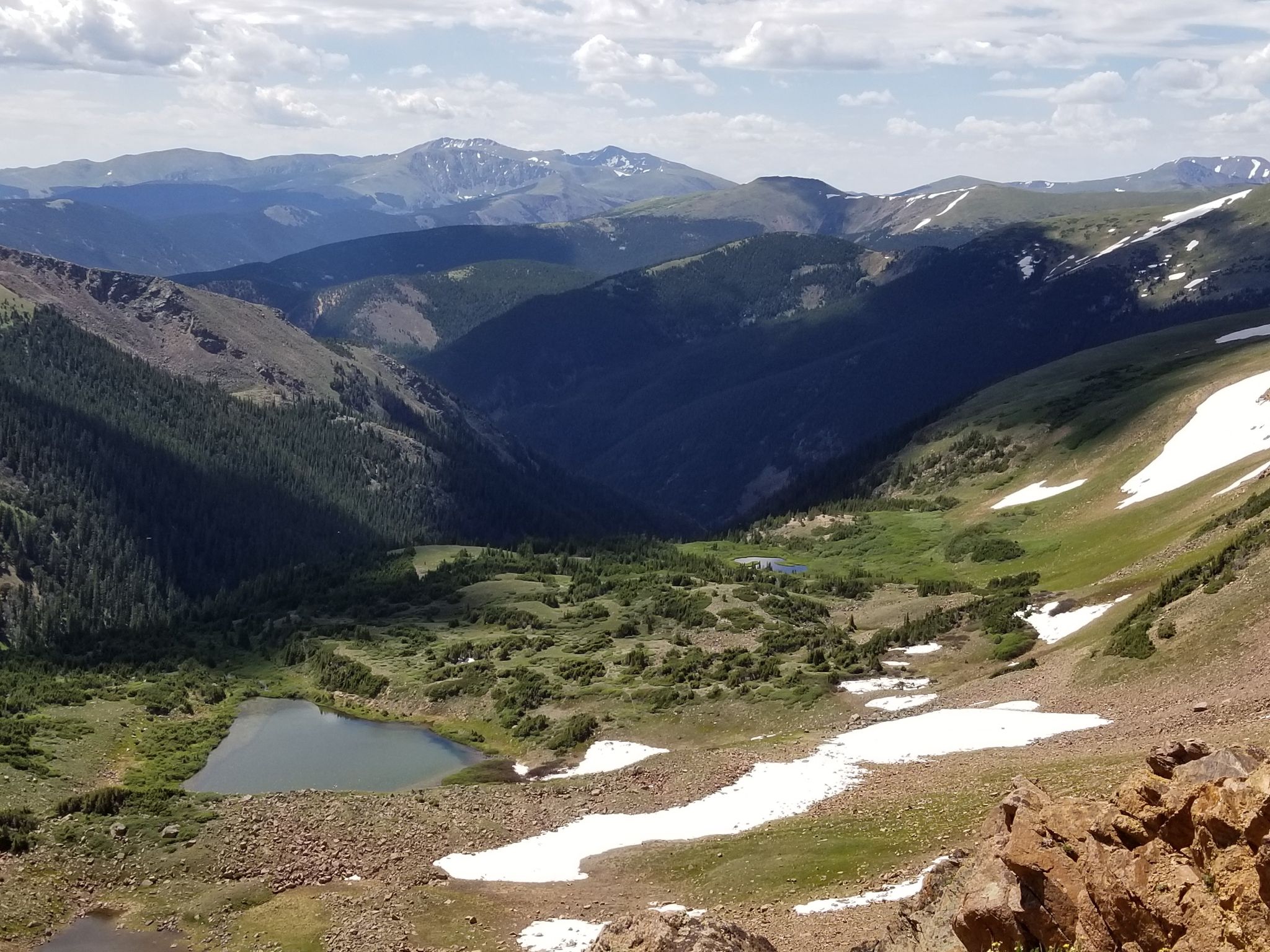Panoramic view of a green mountain valley with a lake and snow patches. - Mount Flora Trail