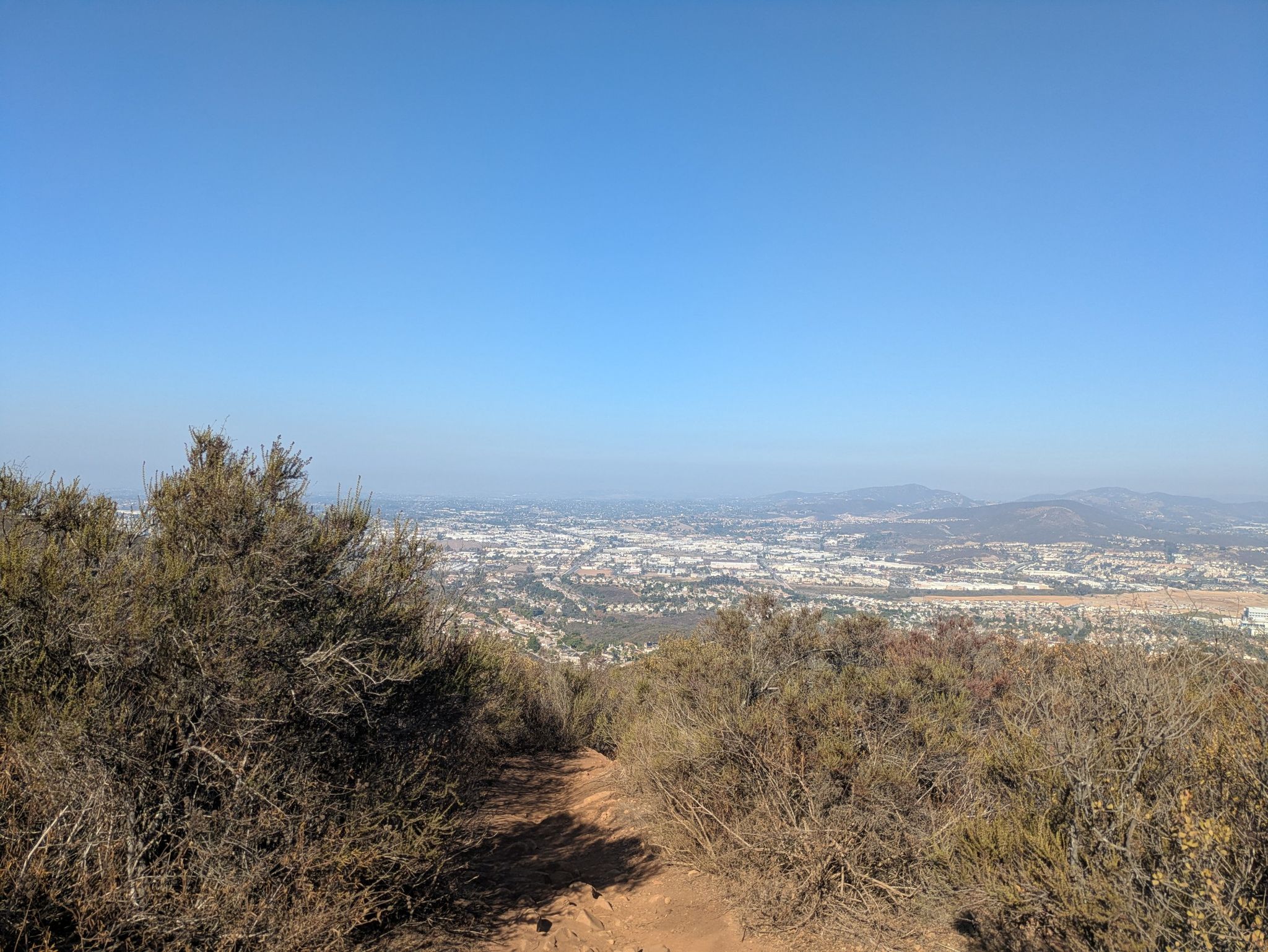 A clear day view of a sprawling city from a brush-covered hillside. - Double Peak Summit View – Double Peak loop from Ridgeline Trailhead