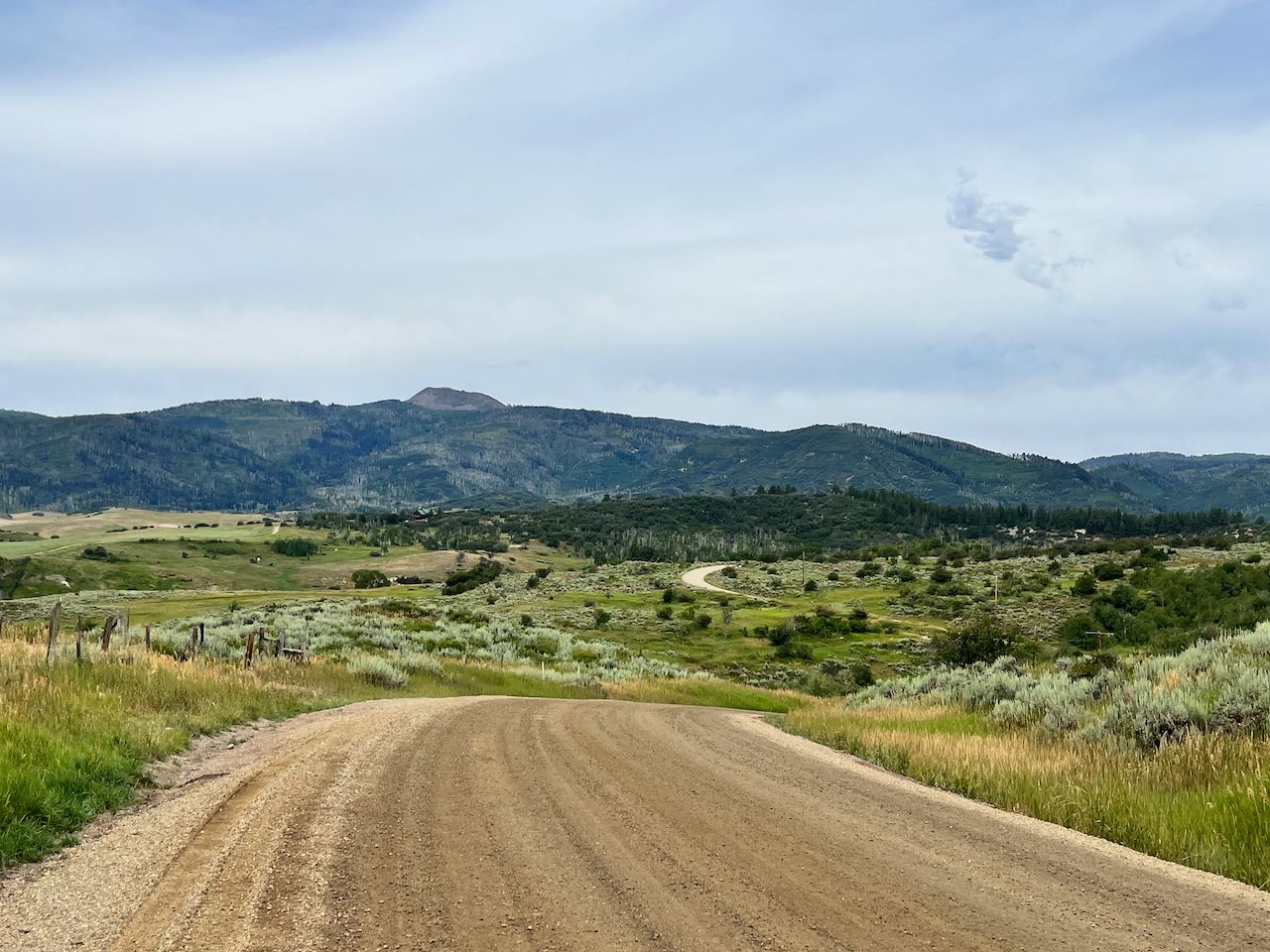 A dirt road winds through rolling green hills towards distant mountains. - Elk River – Yampa riverside park loop from Steamboat 2