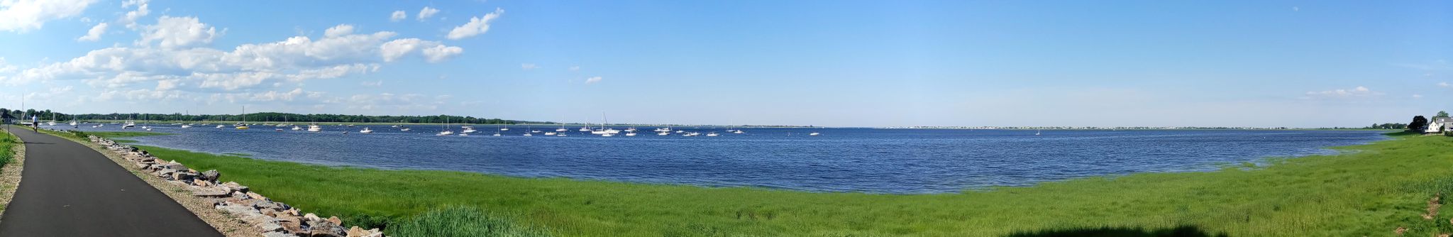 Panoramic view of a wide bay with many boats, green grass, and a paved path. - Hidden Creek Trail – Clipper City Rail Trail loop from Knockers Hole