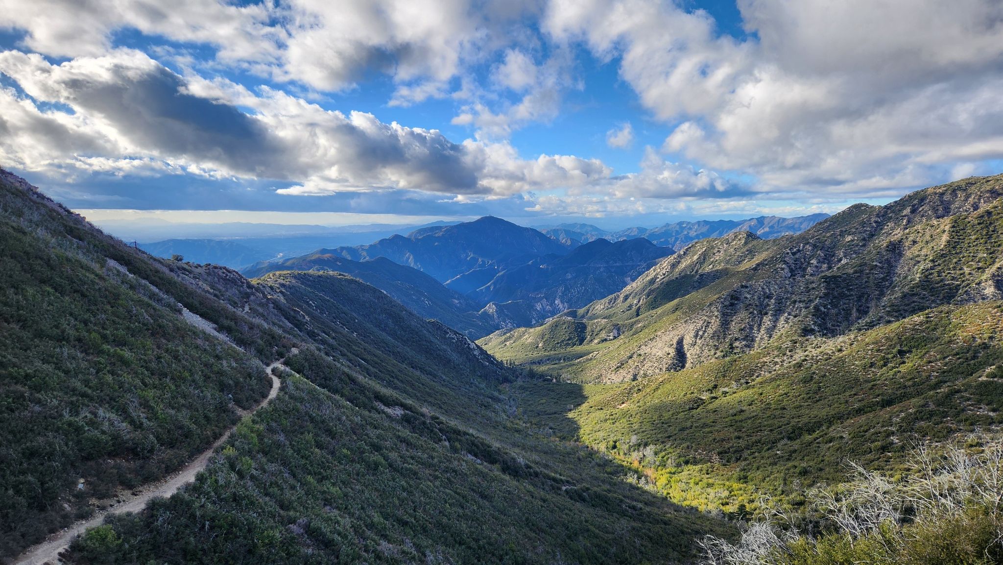 Lush green mountain valley with a winding trail under cloudy sky. - Eaton Saddle to El Prieto Shuttle