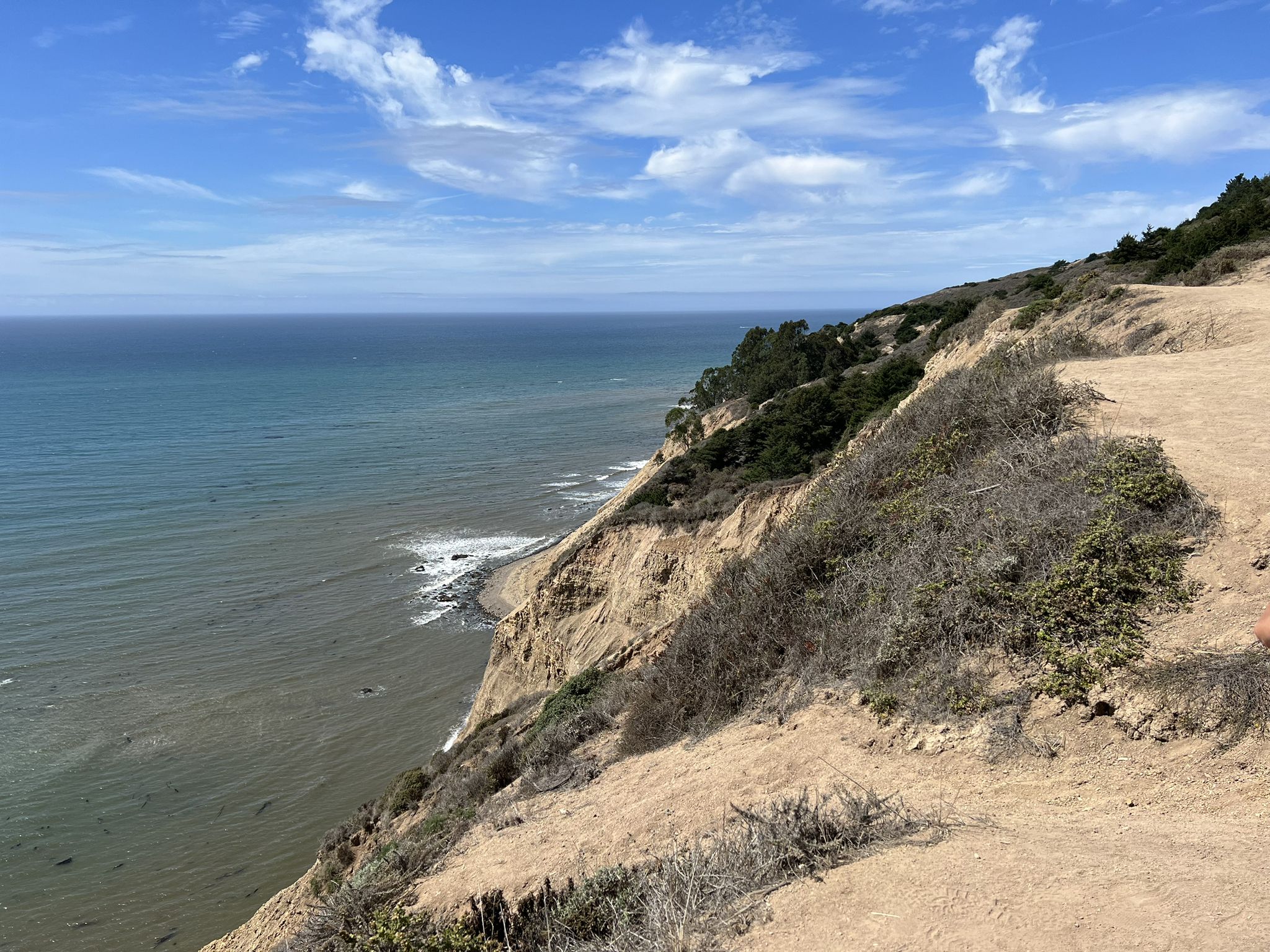 A steep, sandy cliff overlooking a vast ocean with waves under a blue sky. - Coast, Lake Ranch, and Ridge Trail Loop