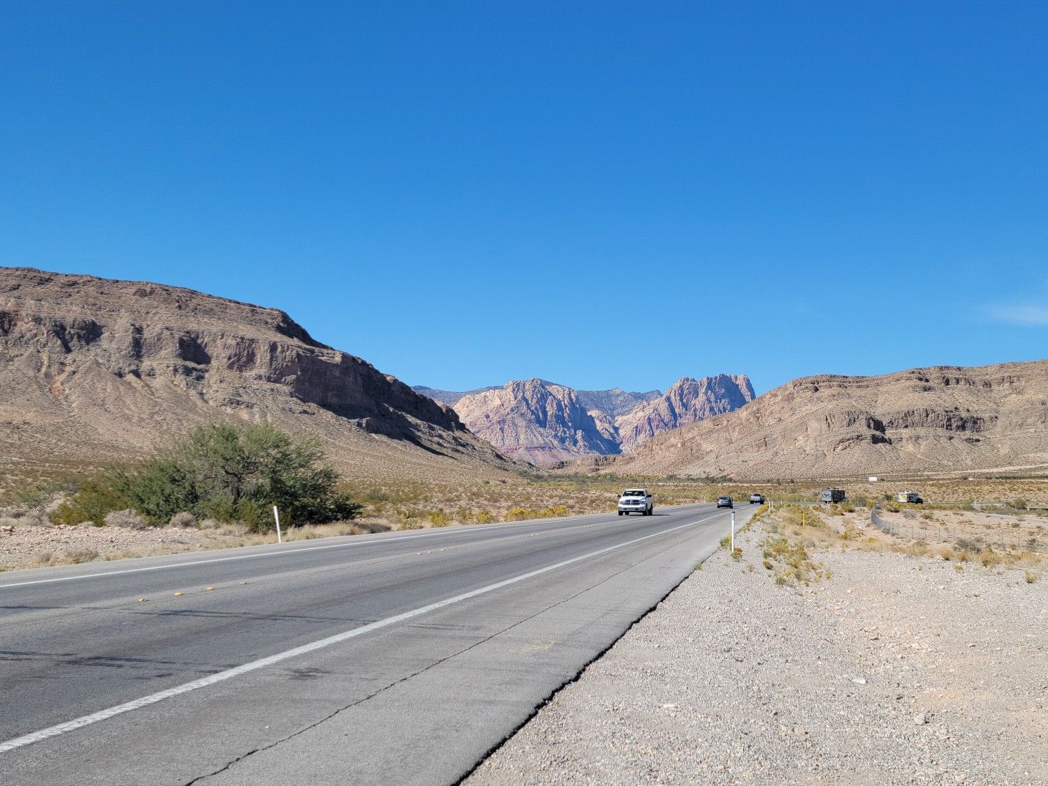A long desert road stretches towards distant mountains under a clear blue sky. - Blue Diamond from Bear's Best Trailhead