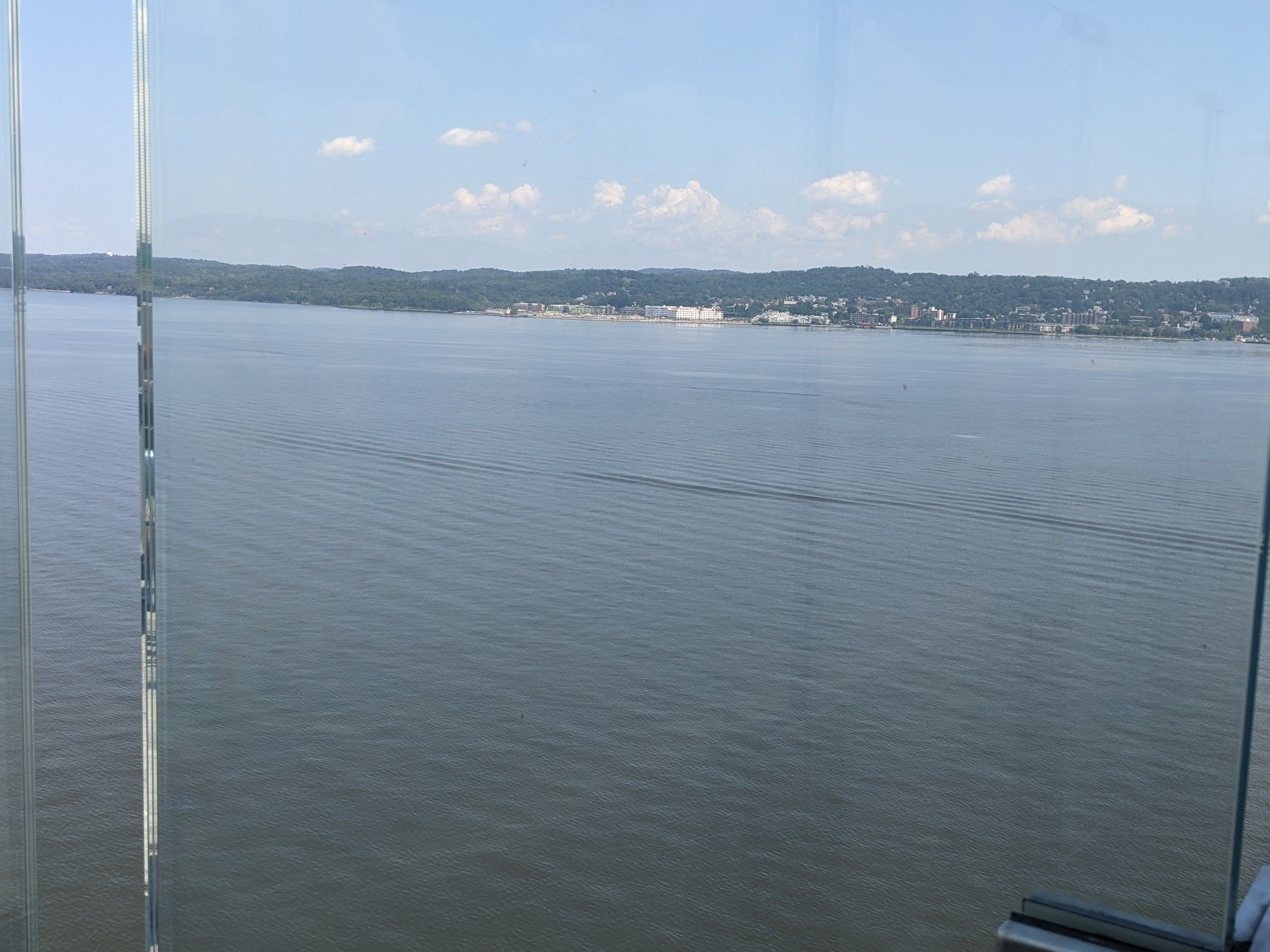 View of a wide body of water and distant hills through a glass barrier. - Painters Point loop from Nyack