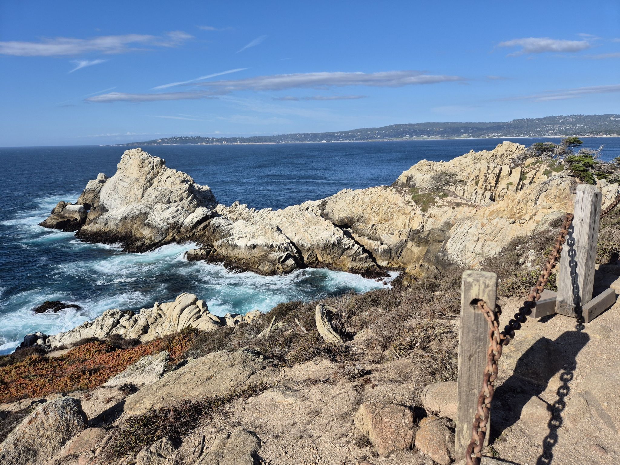 Sunny coastal view with rugged rock formations, crashing waves, and a chain fence. - Cypress Grove Trail