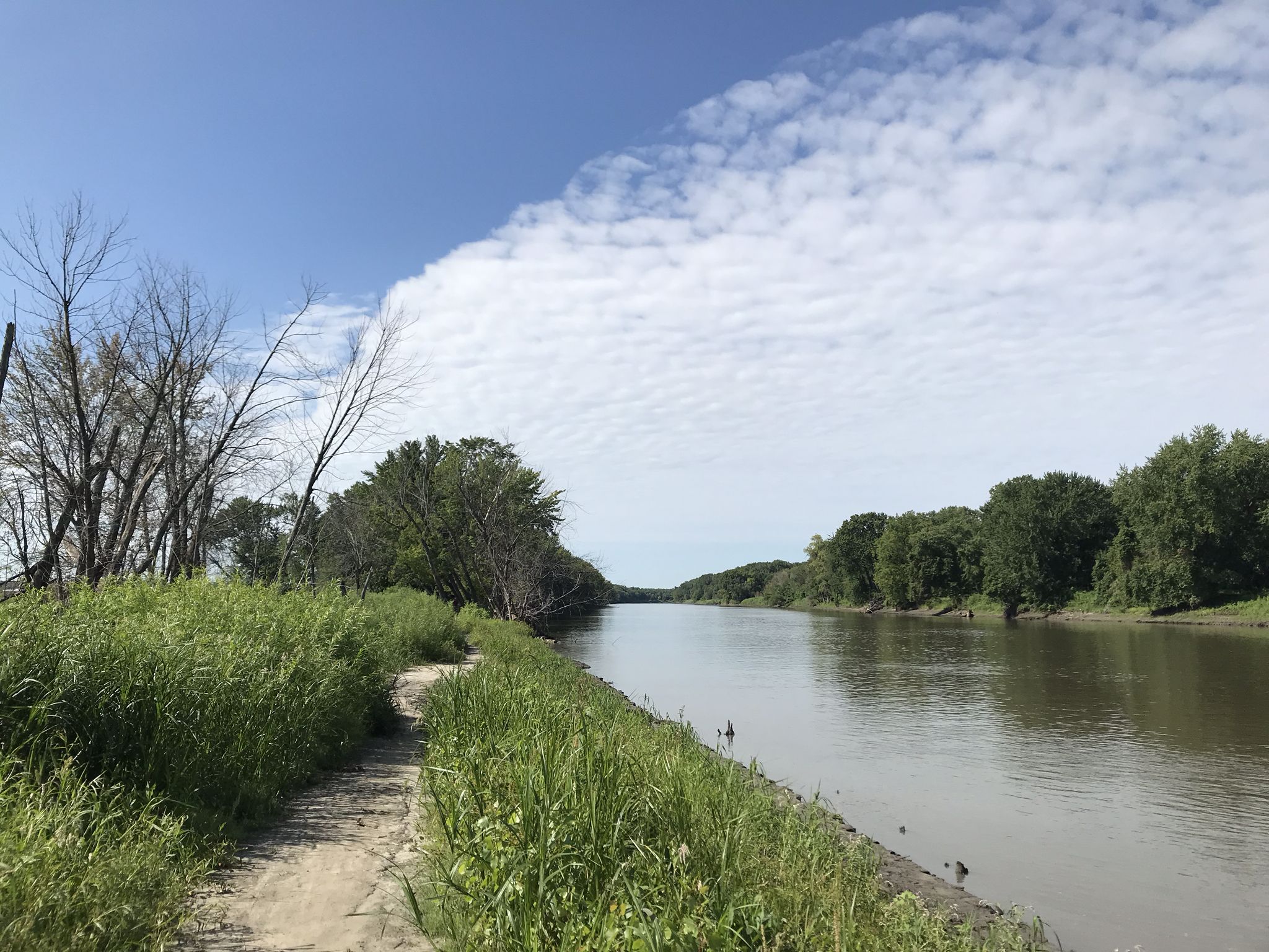 A dirt path runs alongside a wide river under a partly cloudy sky. - Minnesota River and Minnesota Zoo from Apple Valley
