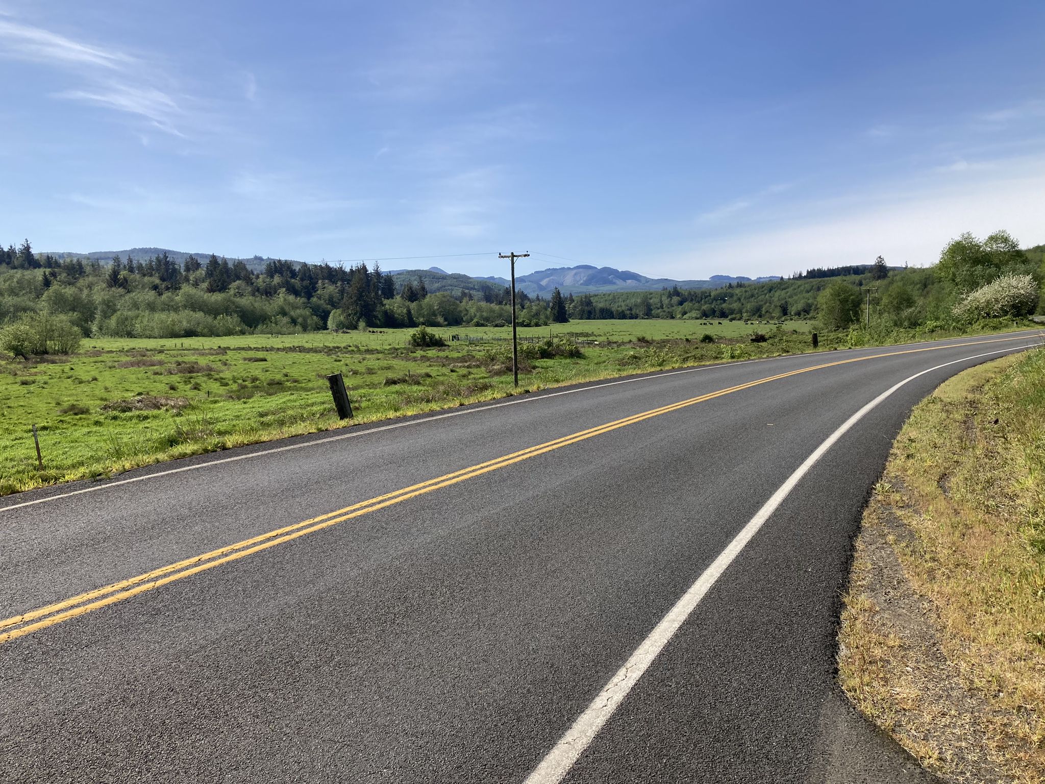 Empty paved road winding through green fields and distant forested mountains. - Youngs River Road loop from Seaside