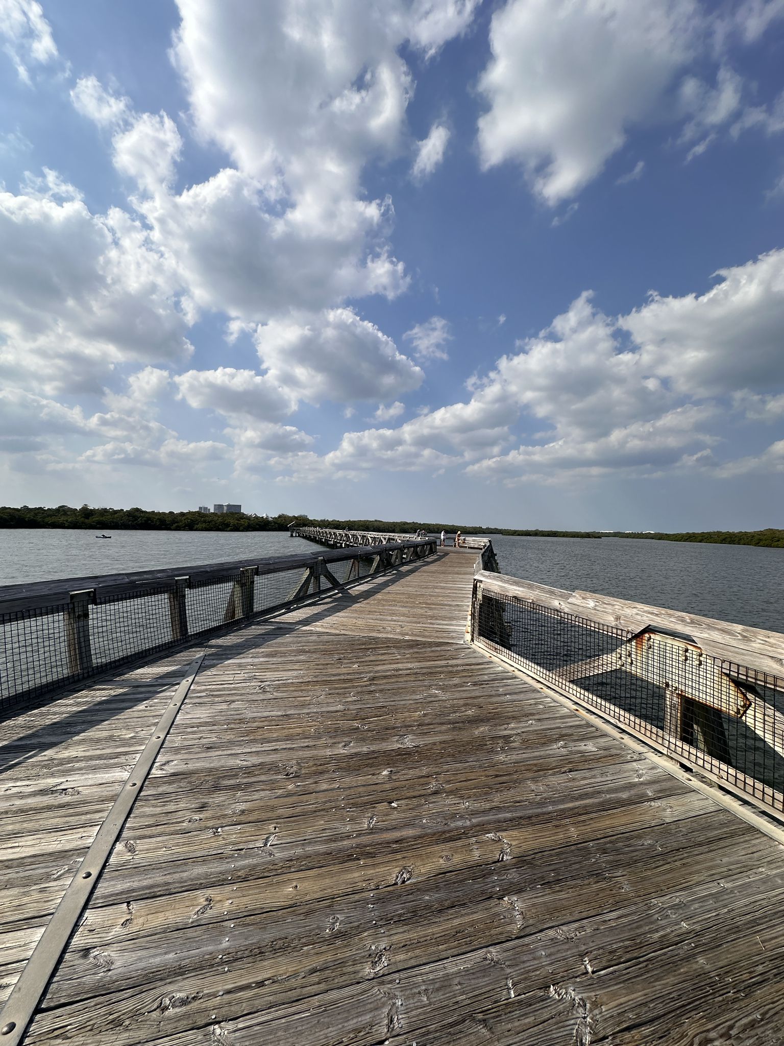 Long wooden boardwalk extends over calm water under a bright, cloudy sky. - John D. MacArthur Beach State Park Boardwalk