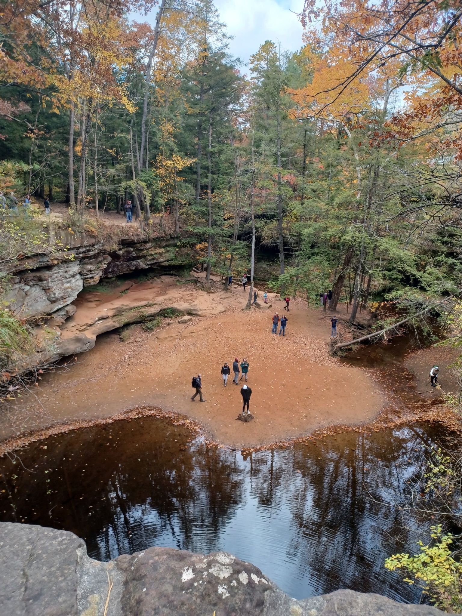 Hikers gathered in a rocky gorge with a pool, surrounded by autumn trees. - Old Man's Cave to Whispering Cave Loop