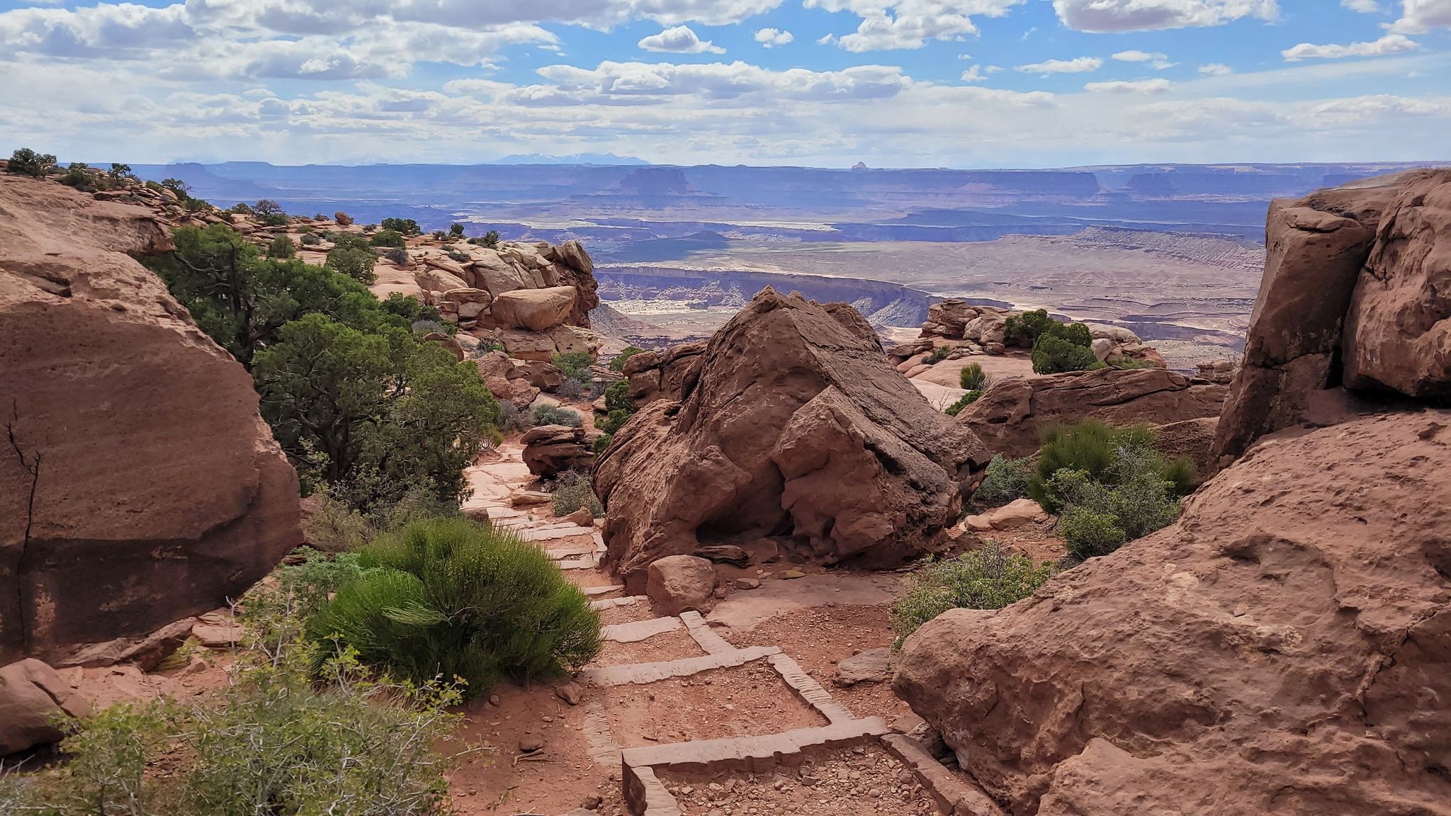Rocky path descending into a vast canyon landscape under a cloudy sky. - Grand View Point Trail