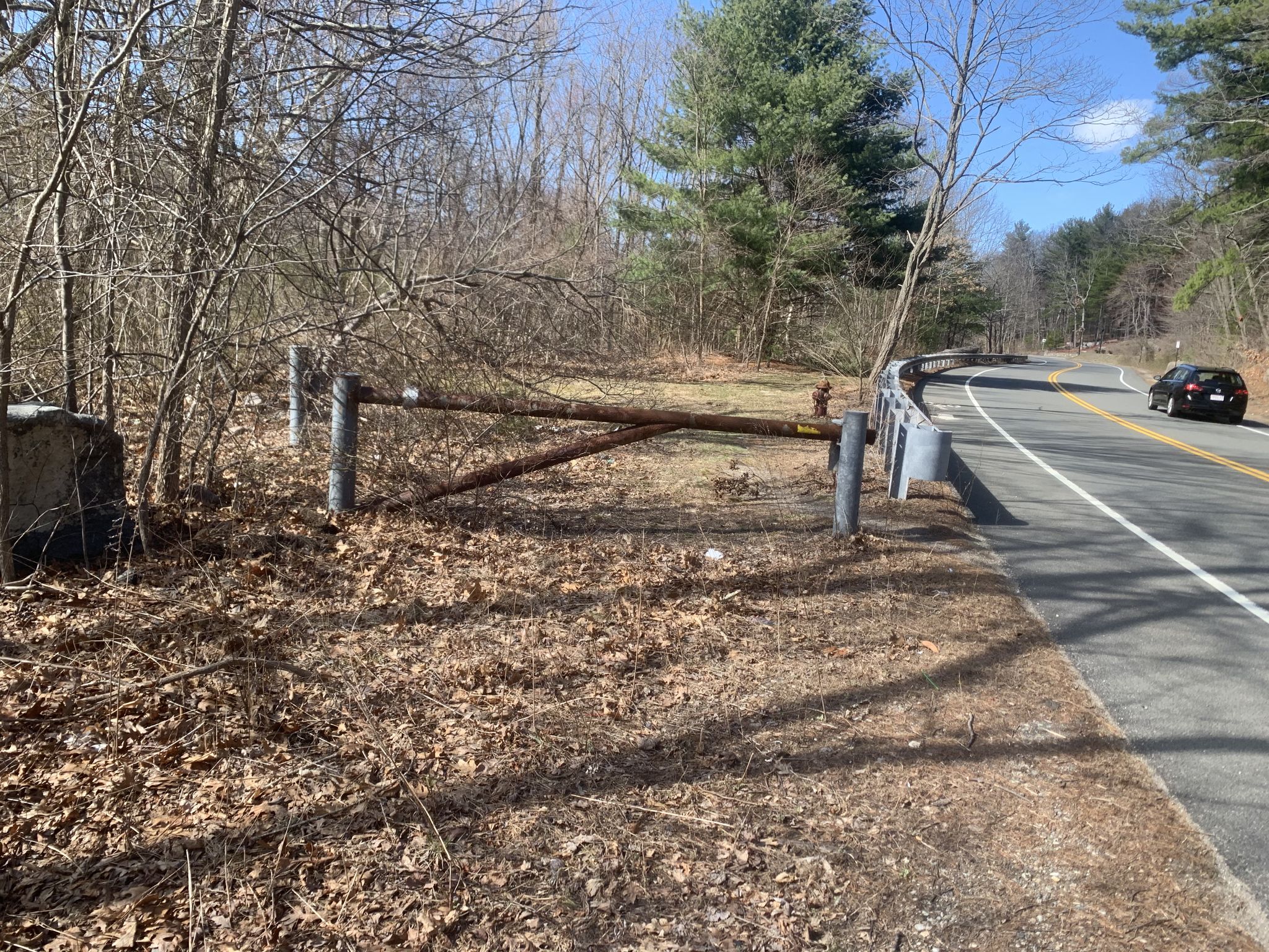 A wooden gate blocks a dirt path next to a sunny road with a distant car. - Peters Hill from Norton via Borderland State Park loop