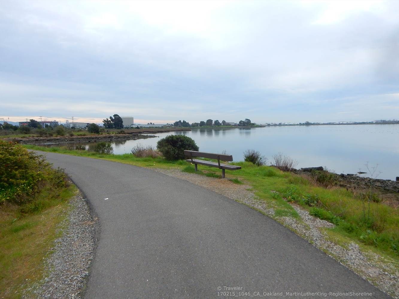 A paved path and bench beside calm water under an overcast sky. - San Francisco Bay Trail Loop