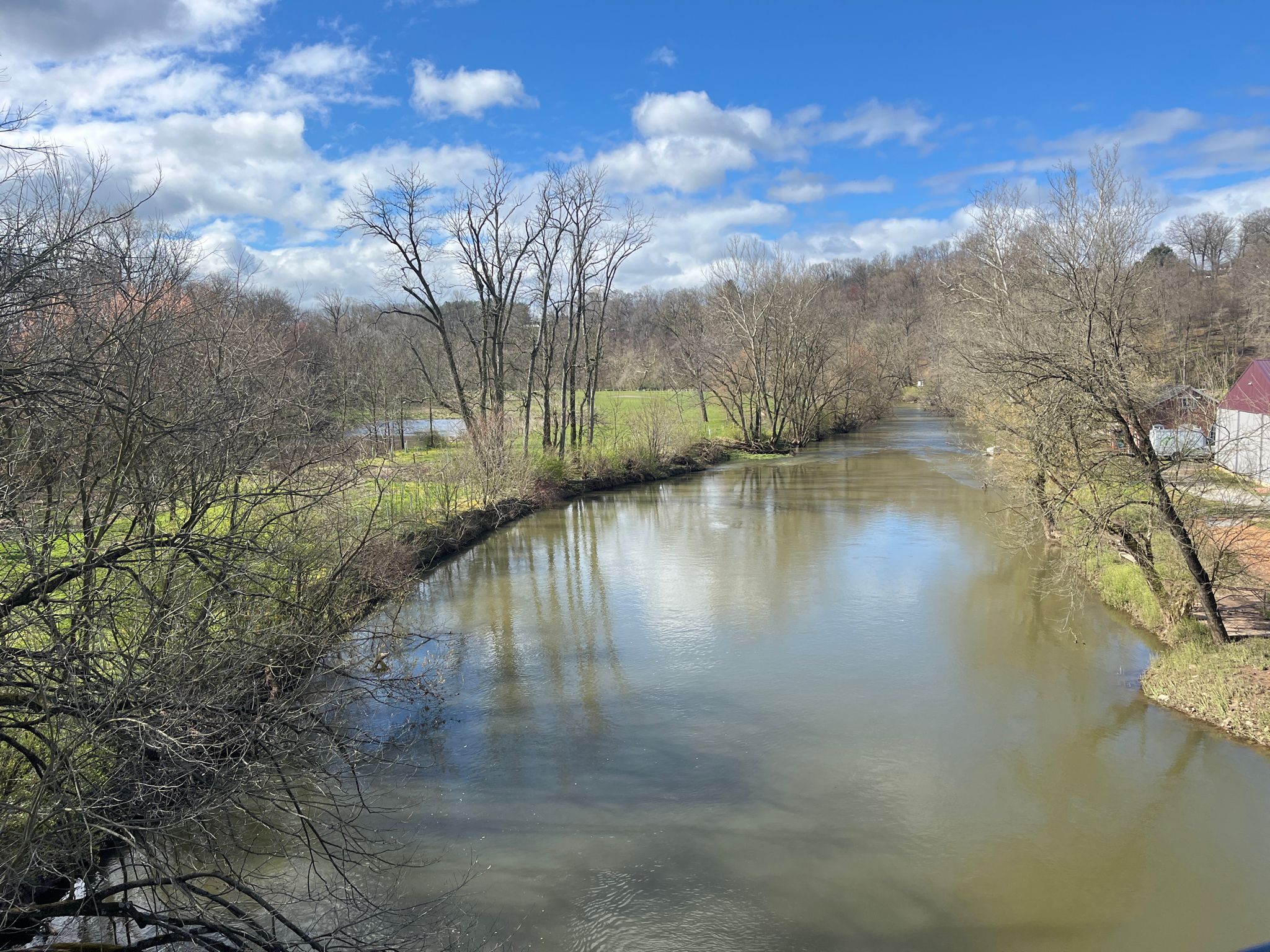 A calm river flows between banks with bare trees under a cloudy sky. - Warwick to Ephrata Rail-Trail