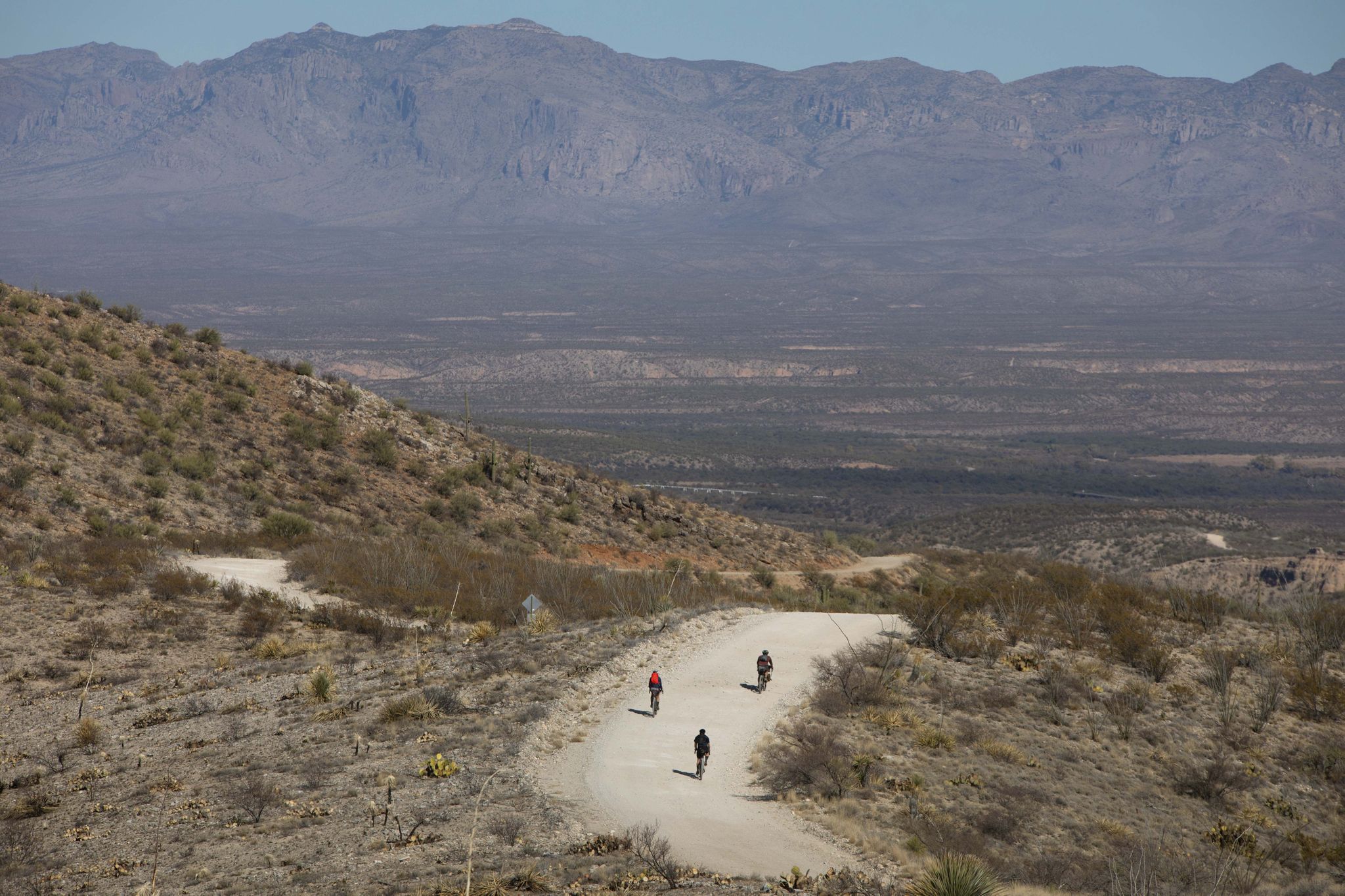 Three people on a winding dirt road overlooking a vast arid valley. - Redington Road FS371