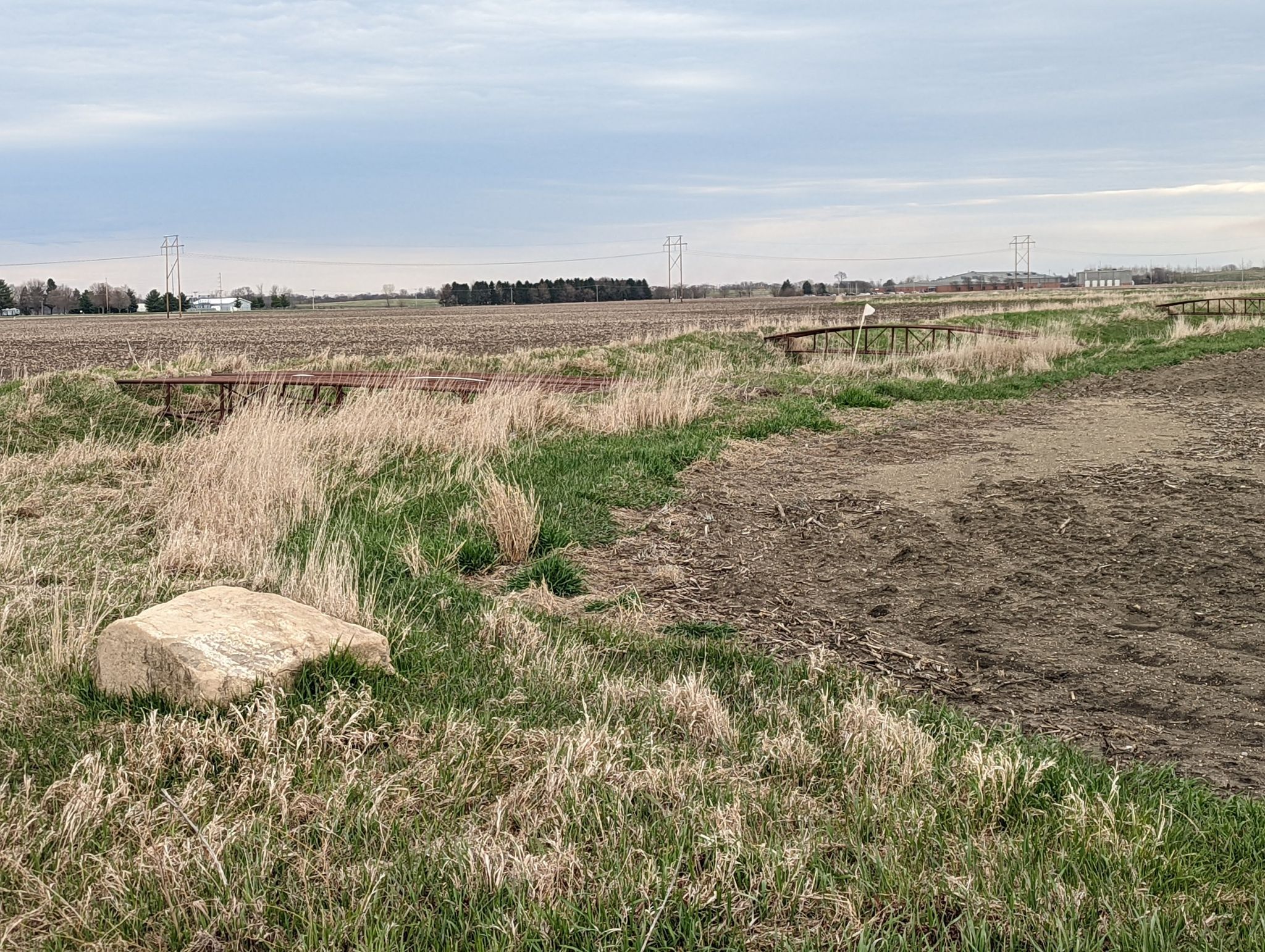 Overcast sky above a flat, grassy field with a large rock and bare dirt. - Urbana to Rantoul