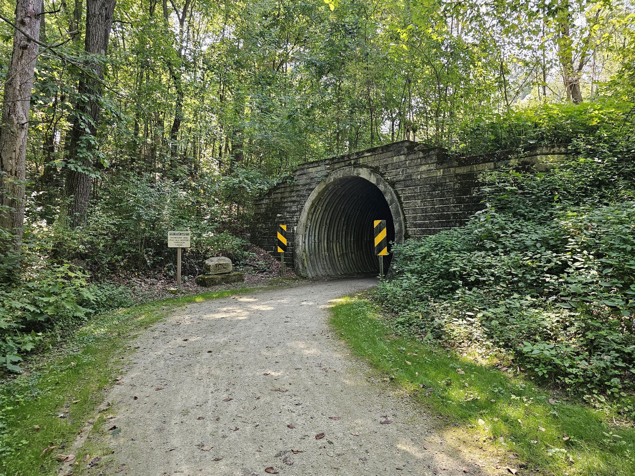 Stone tunnel entrance on a dirt path, surrounded by dense green trees. - Large Sycamore loop from McDonnell Trailhead