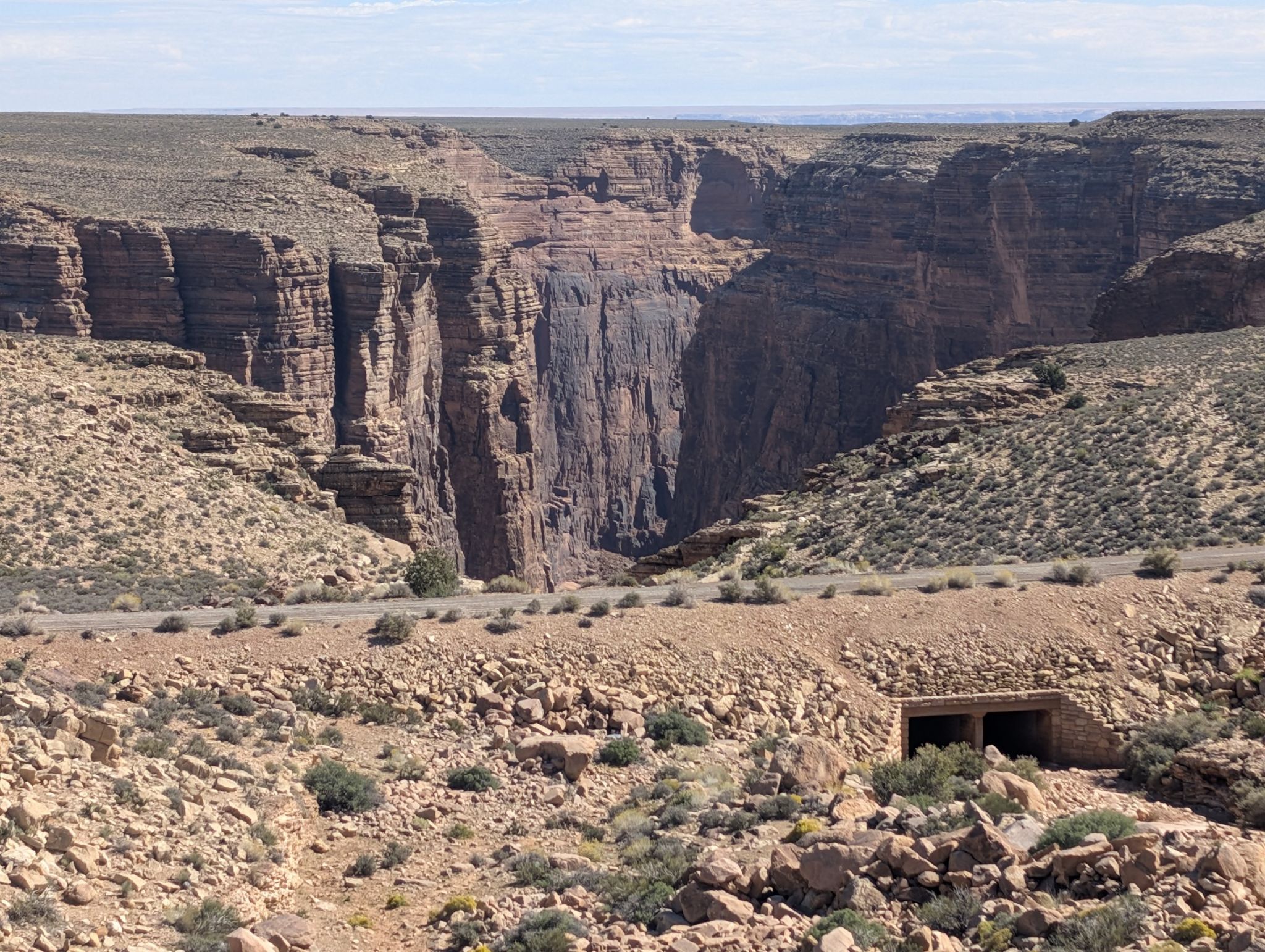 Deep canyon with steep rock walls, a road, and a culvert under clear skies. - Desert View Scenic Drive