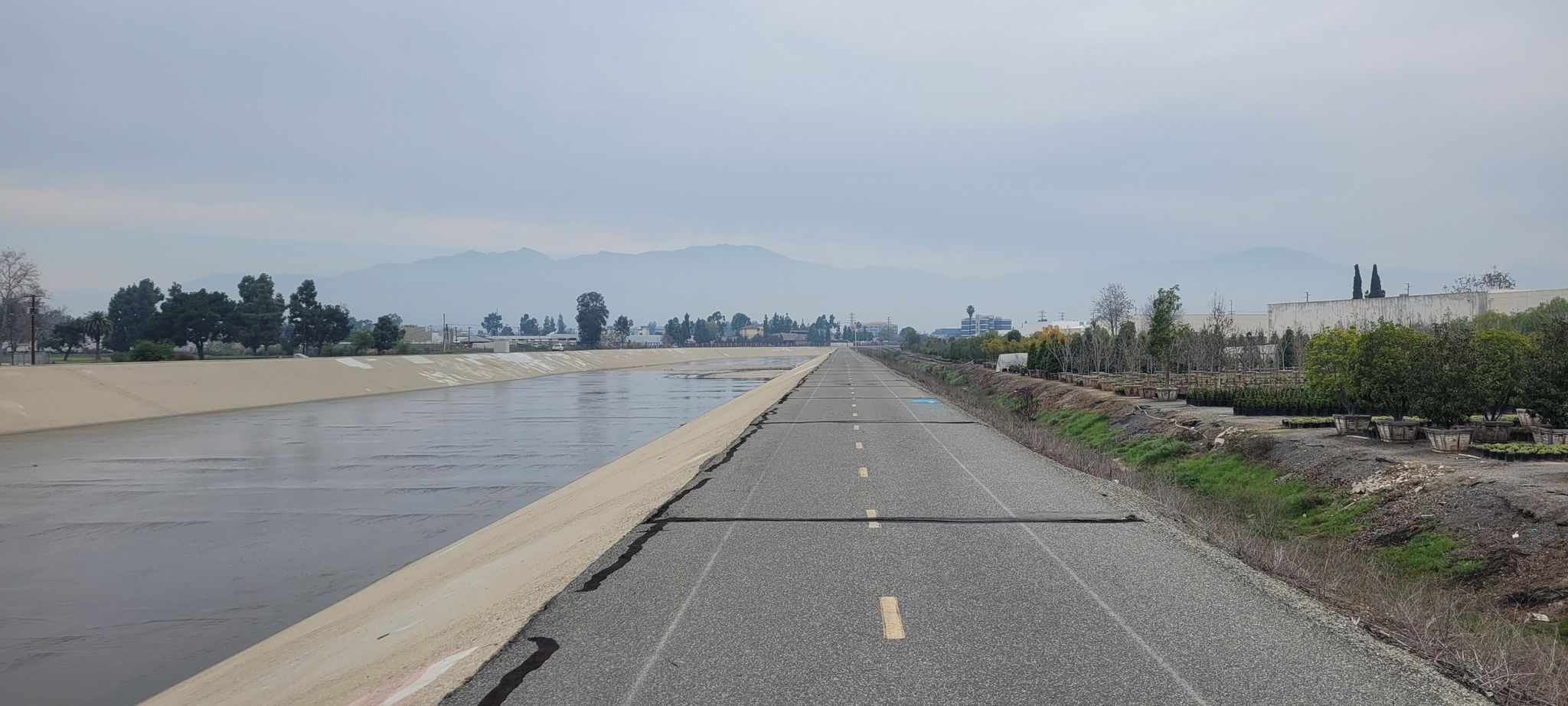 A paved path runs next to a wide concrete canal with distant mountains. - Bosque del Rio Hondo – Rio Hondo Greenway loop from West Whittier